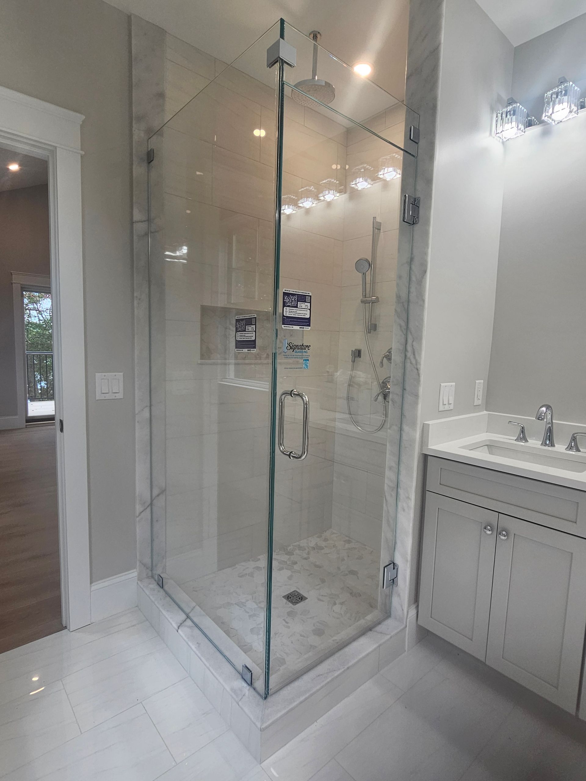Glass shower enclosure in a bathroom with white tile and vanity.