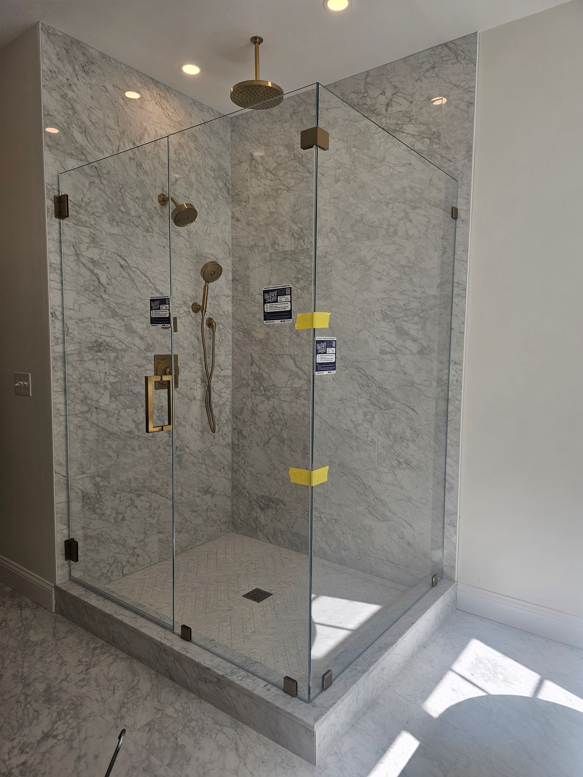 Corner shower with marble walls, glass doors, and gold fixtures.