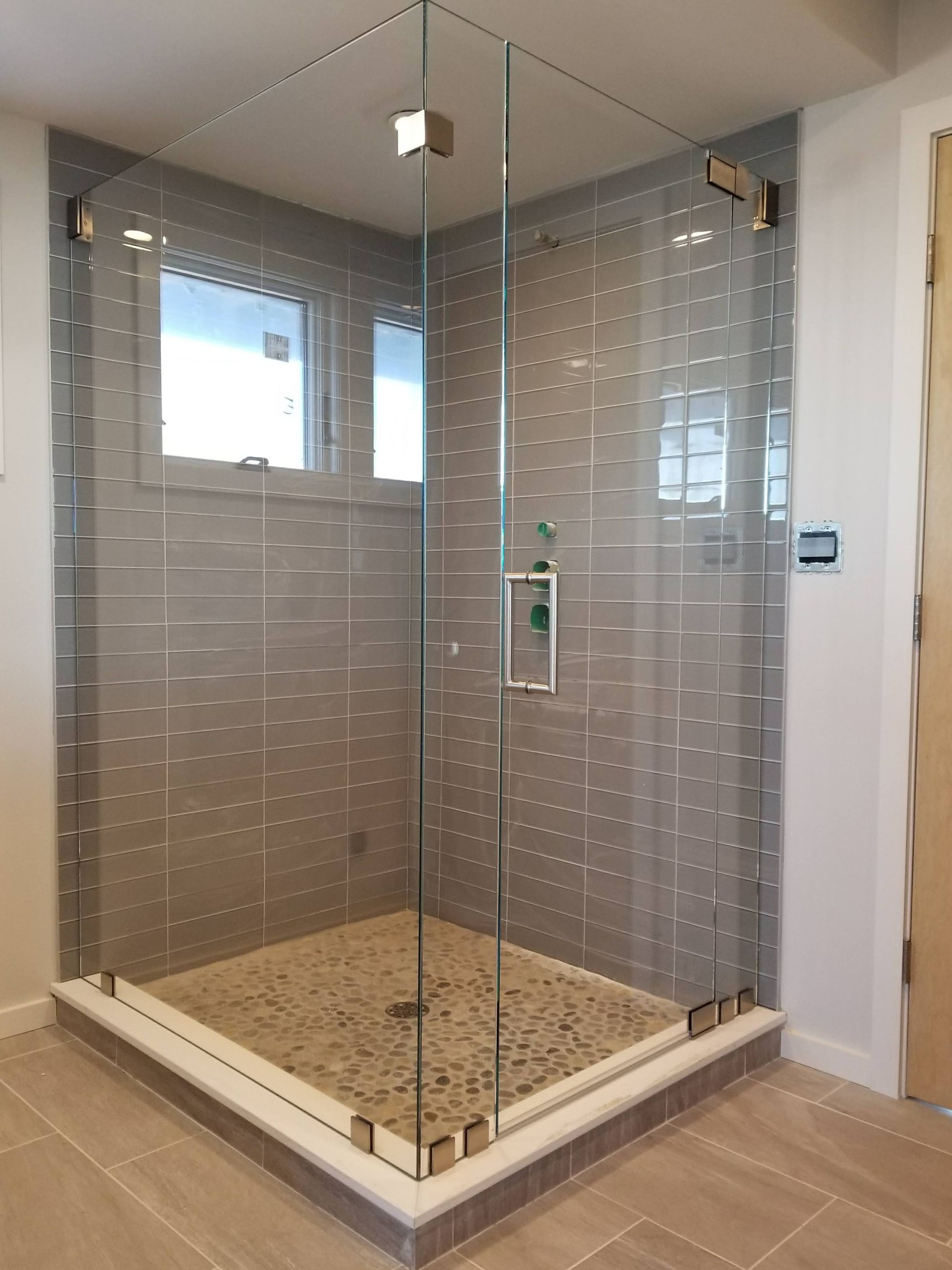 Glass shower enclosure in a bathroom with gray tile walls and a pebble floor.