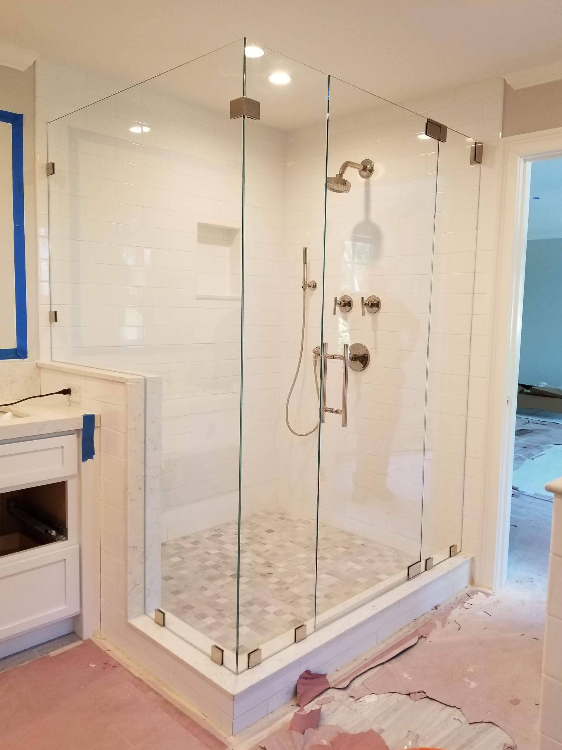 Glass-enclosed shower in a newly renovated bathroom with white tile walls and a stone floor.