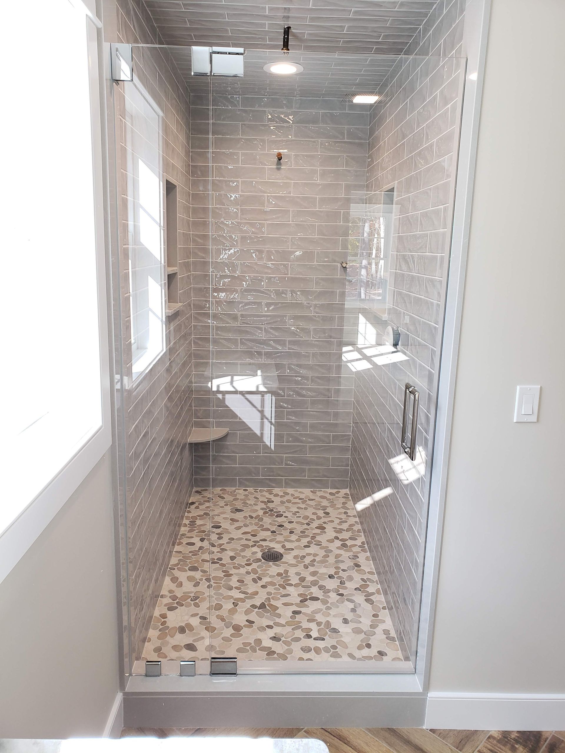 Glass-walled shower with gray brick-like tile, pebble floor, and white trim. Includes a small built-in bench.