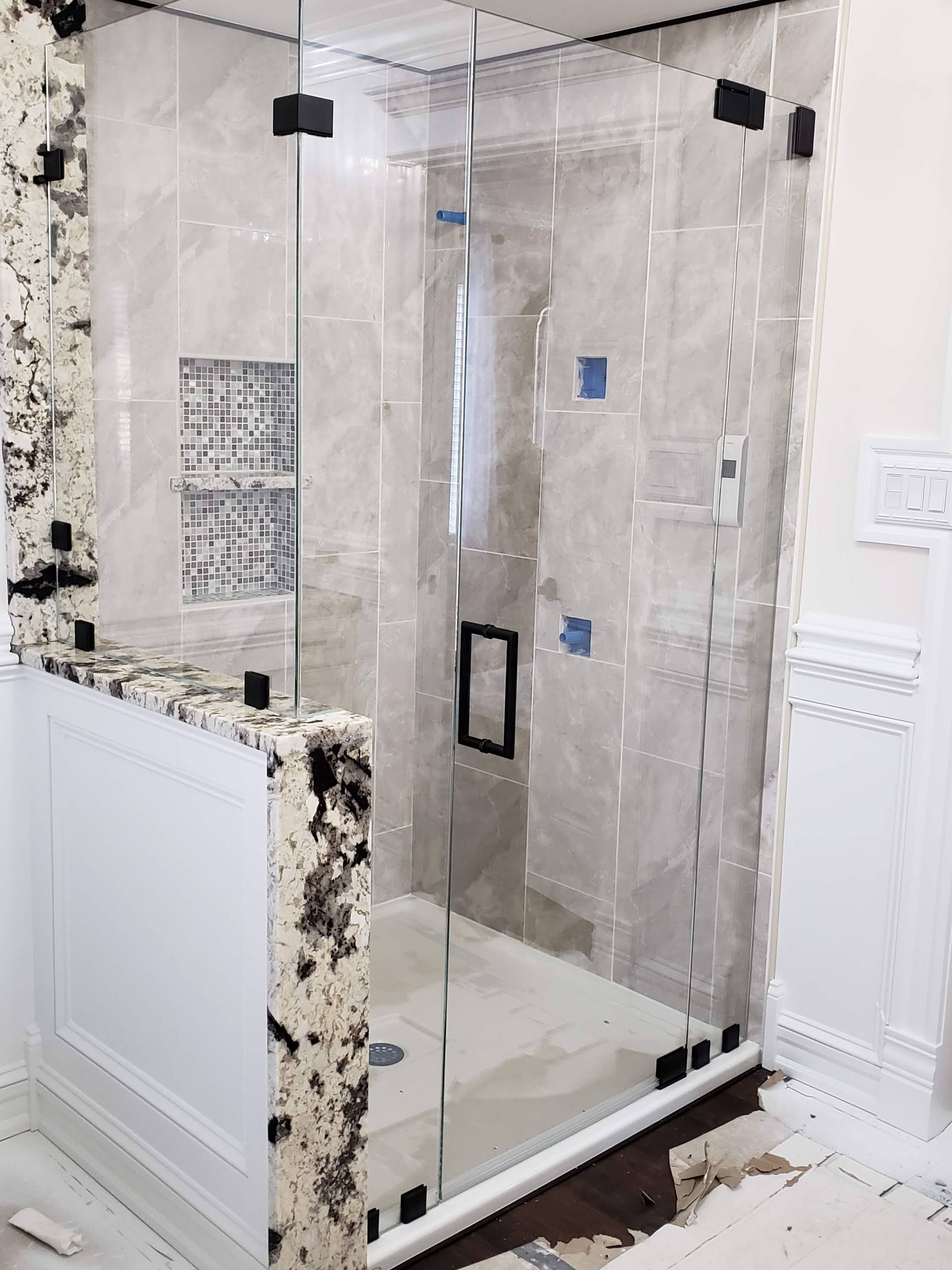 Glass shower enclosure with black hinges in a tiled bathroom.