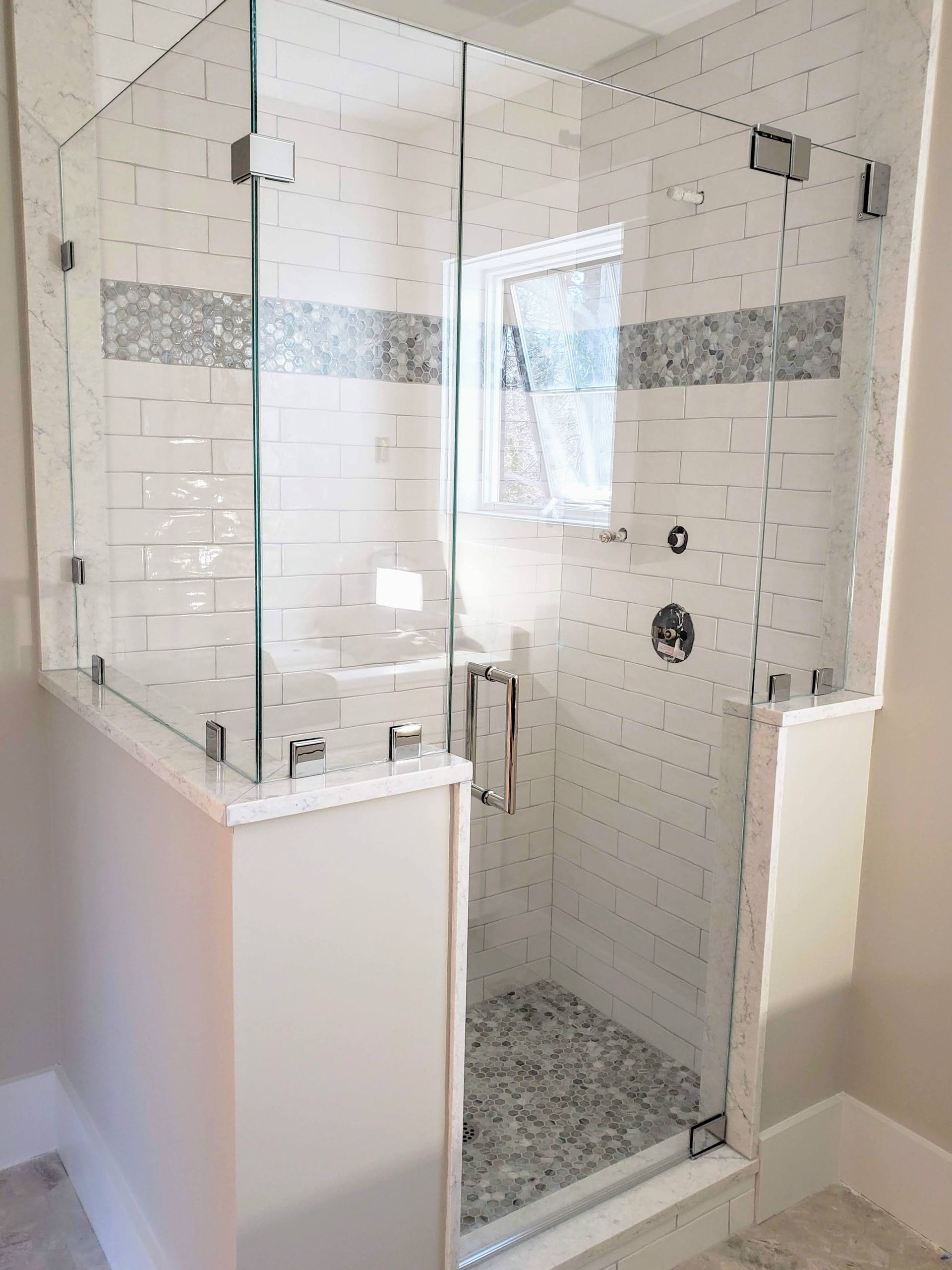 Glass shower enclosure with white tile walls and pebble floor.