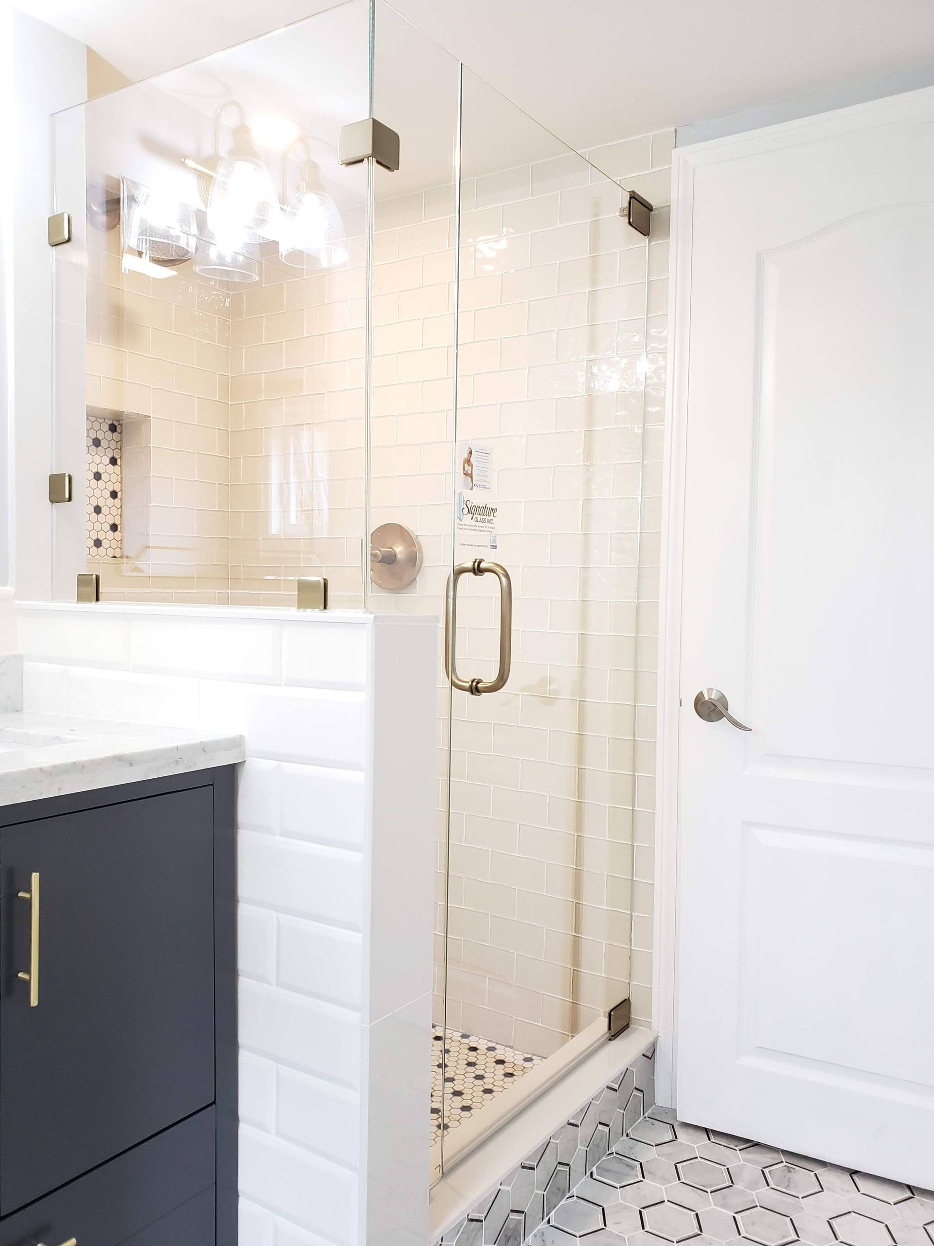 Glass shower with white tile, gold hardware, and a dark cabinet.