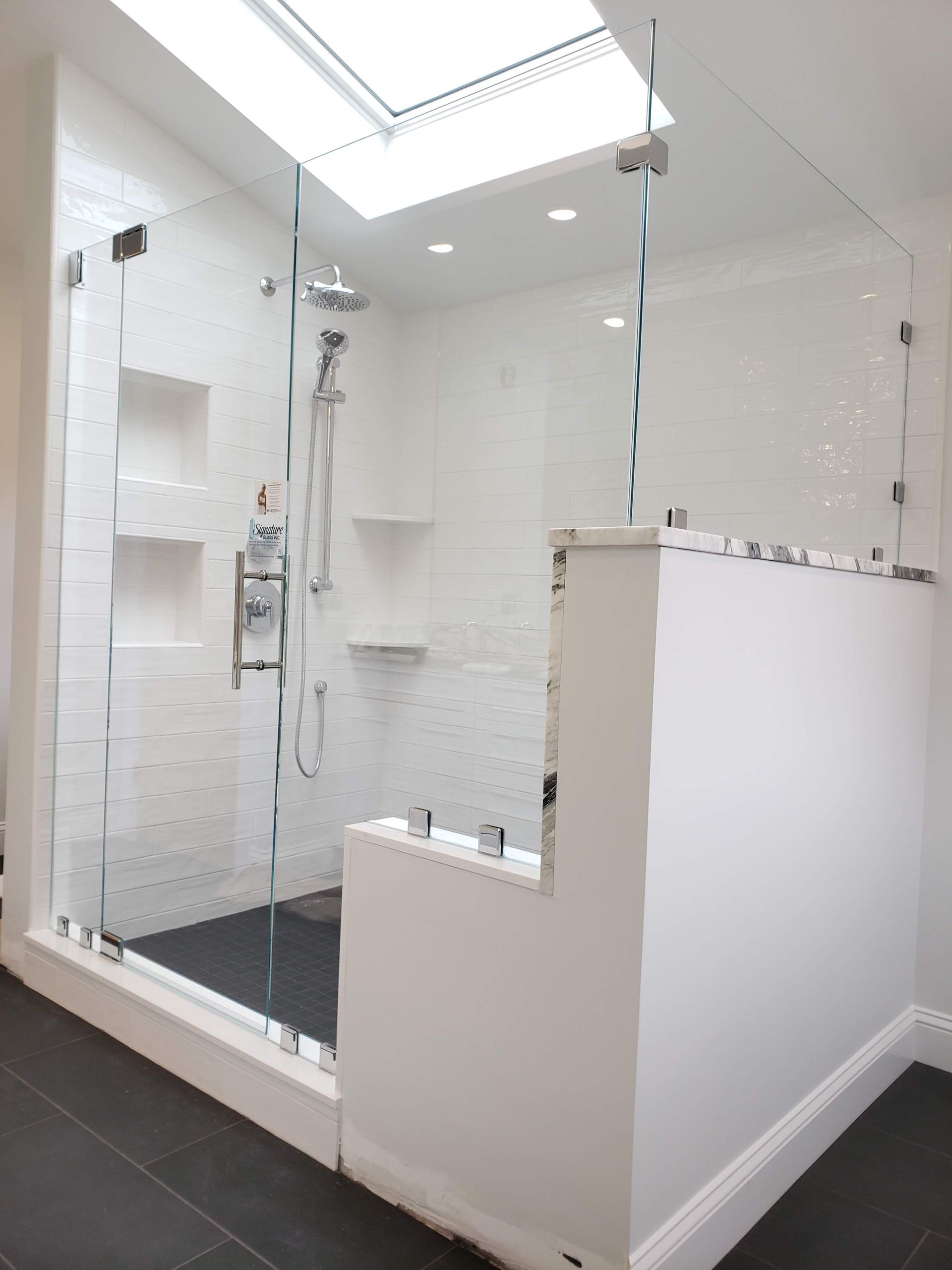 Modern white tiled shower with glass doors and a skylight.