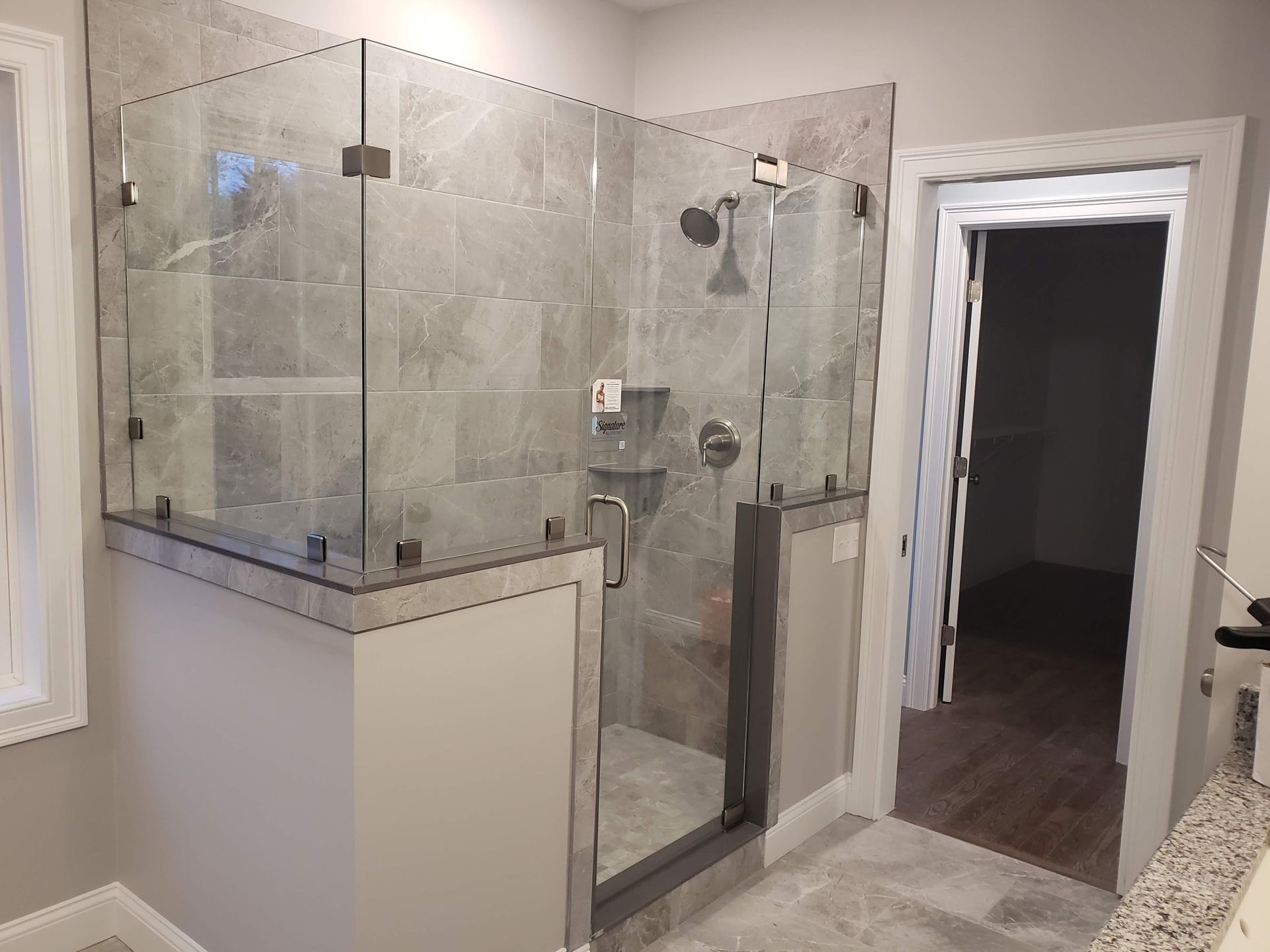 Modern gray tiled shower with glass doors and chrome fixtures, adjacent to a doorway.