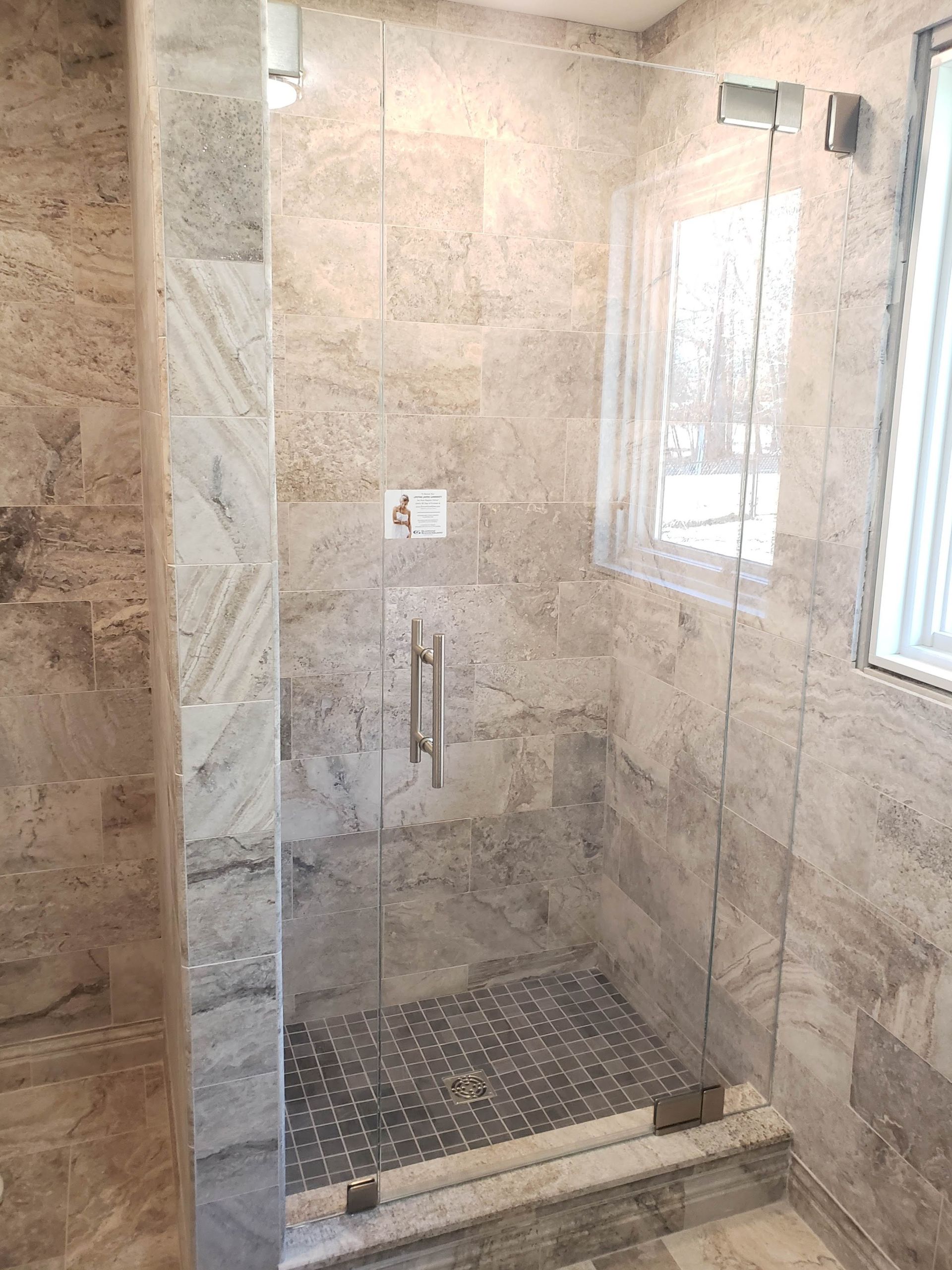 Glass shower with stone tile walls and a pebble floor, a window is visible.