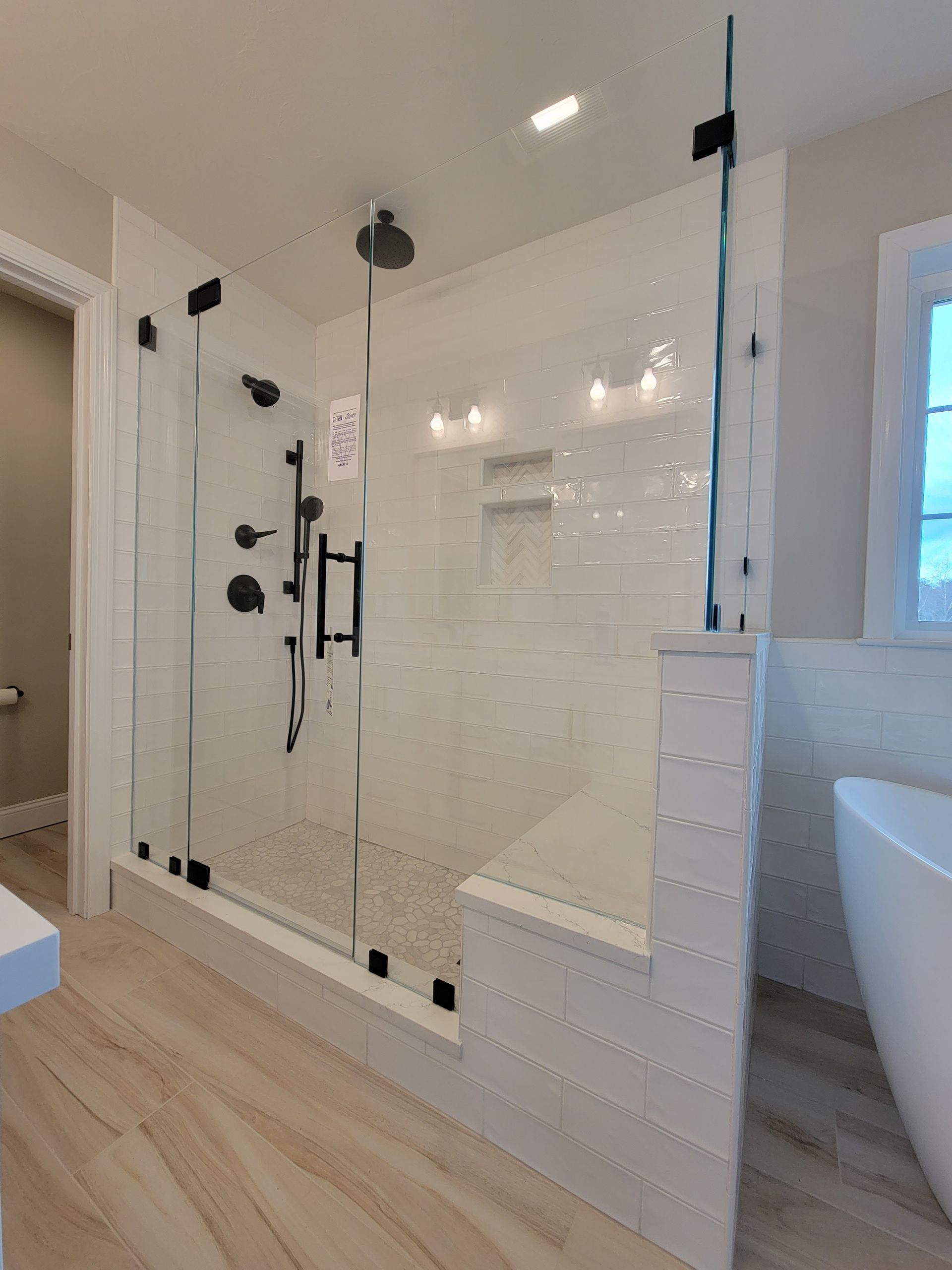 Modern bathroom with glass shower enclosure, black fixtures, and white tile.