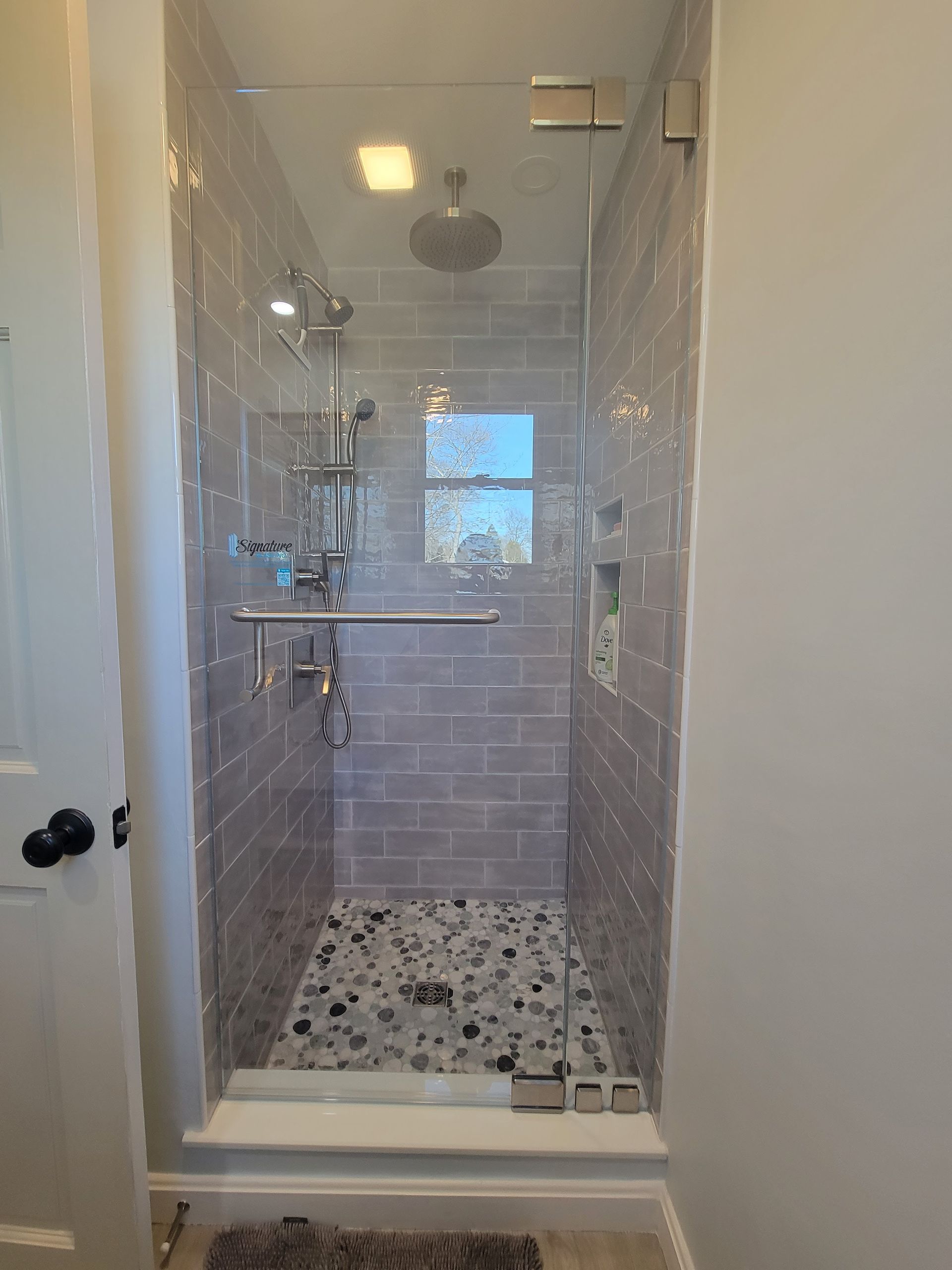Shower stall with gray tile, pebble floor, and glass door.