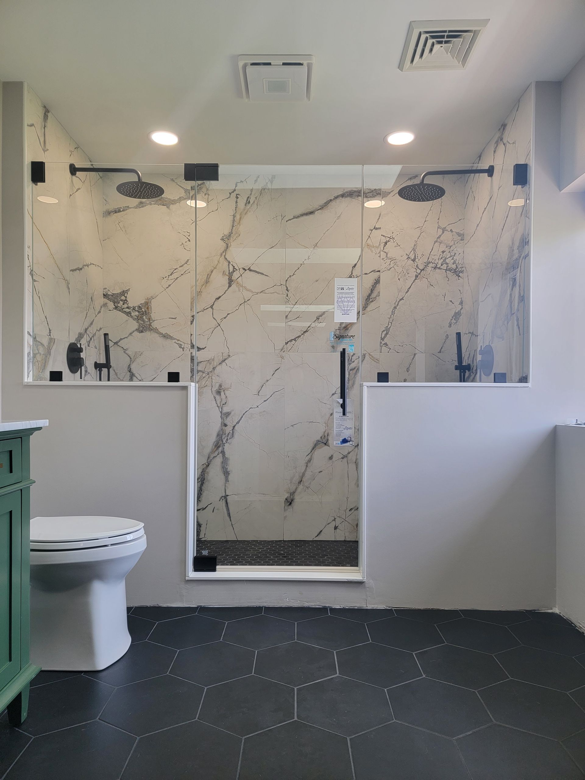 Bathroom with marble-look shower and black hexagon tile floor; toilet and green vanity visible.