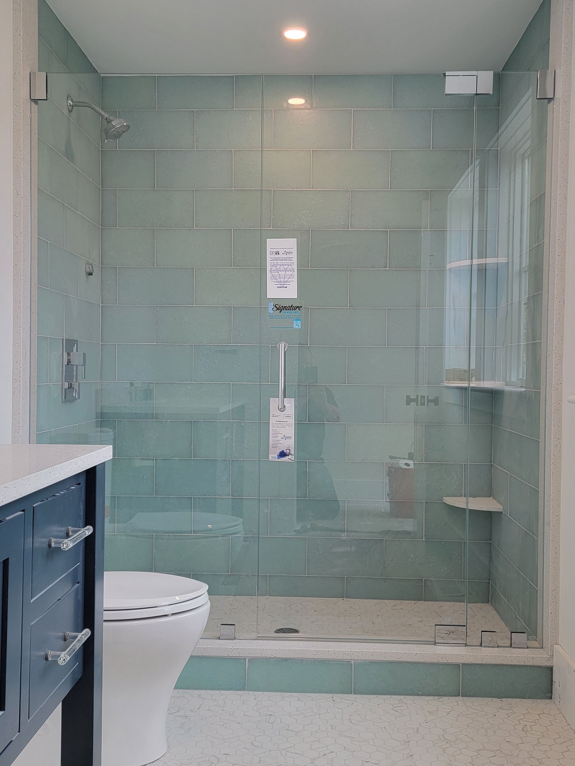 Bathroom with a blue tiled shower, glass door, and white vanity.