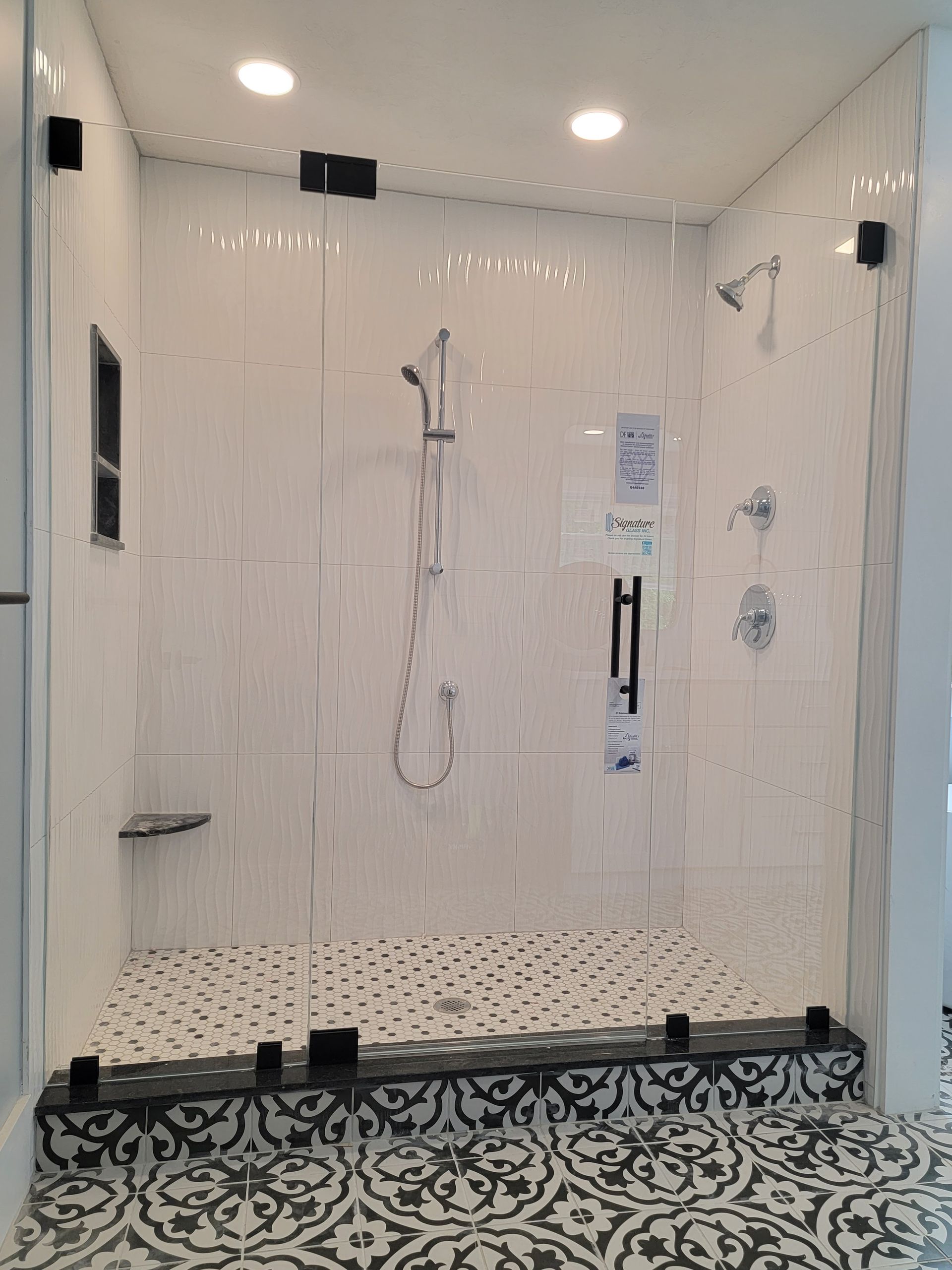 Modern shower with white tiled walls, glass doors, and black and white patterned floor tiles.