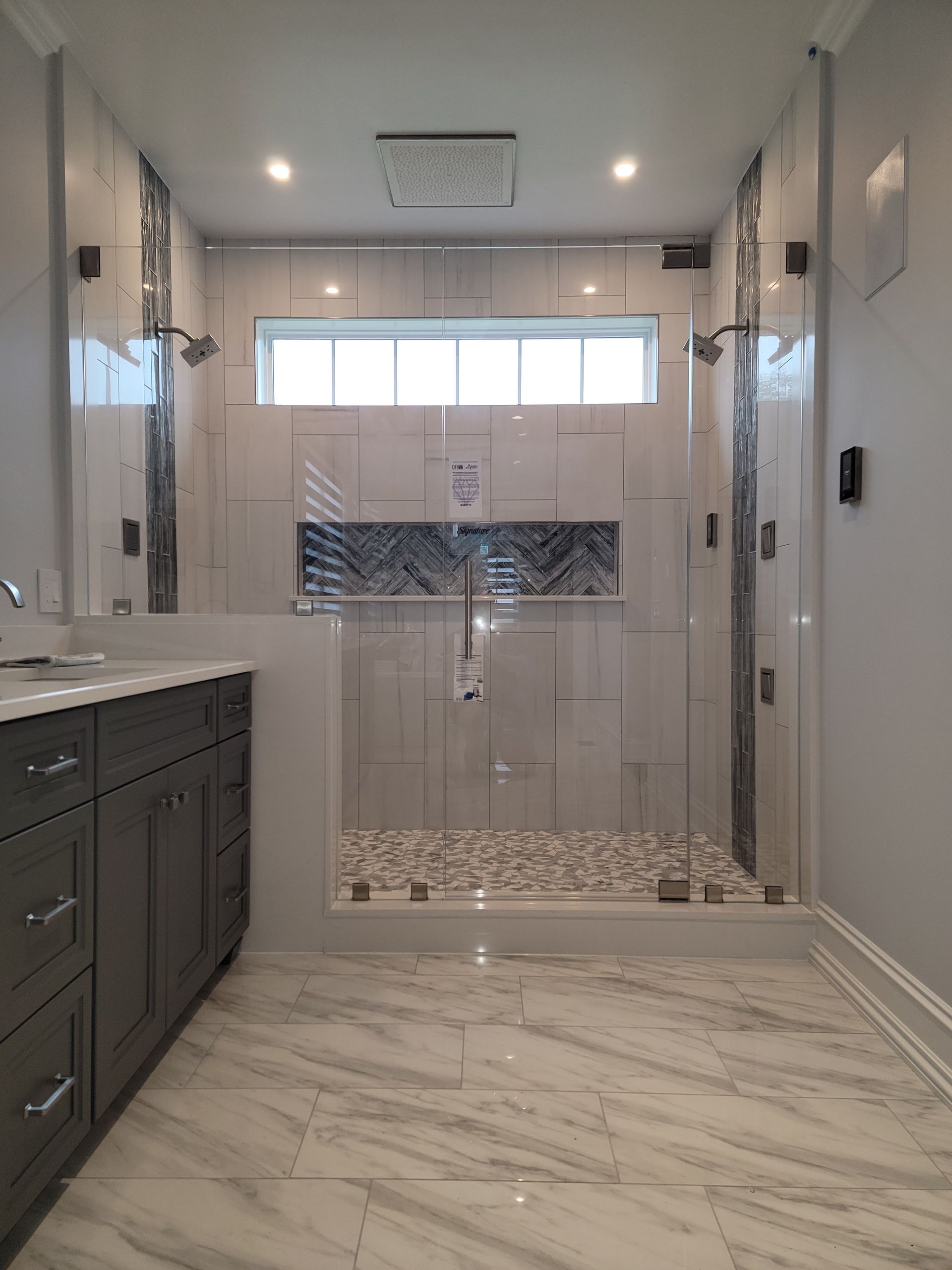 Luxurious bathroom with a glass shower, marble tile, and gray vanity.