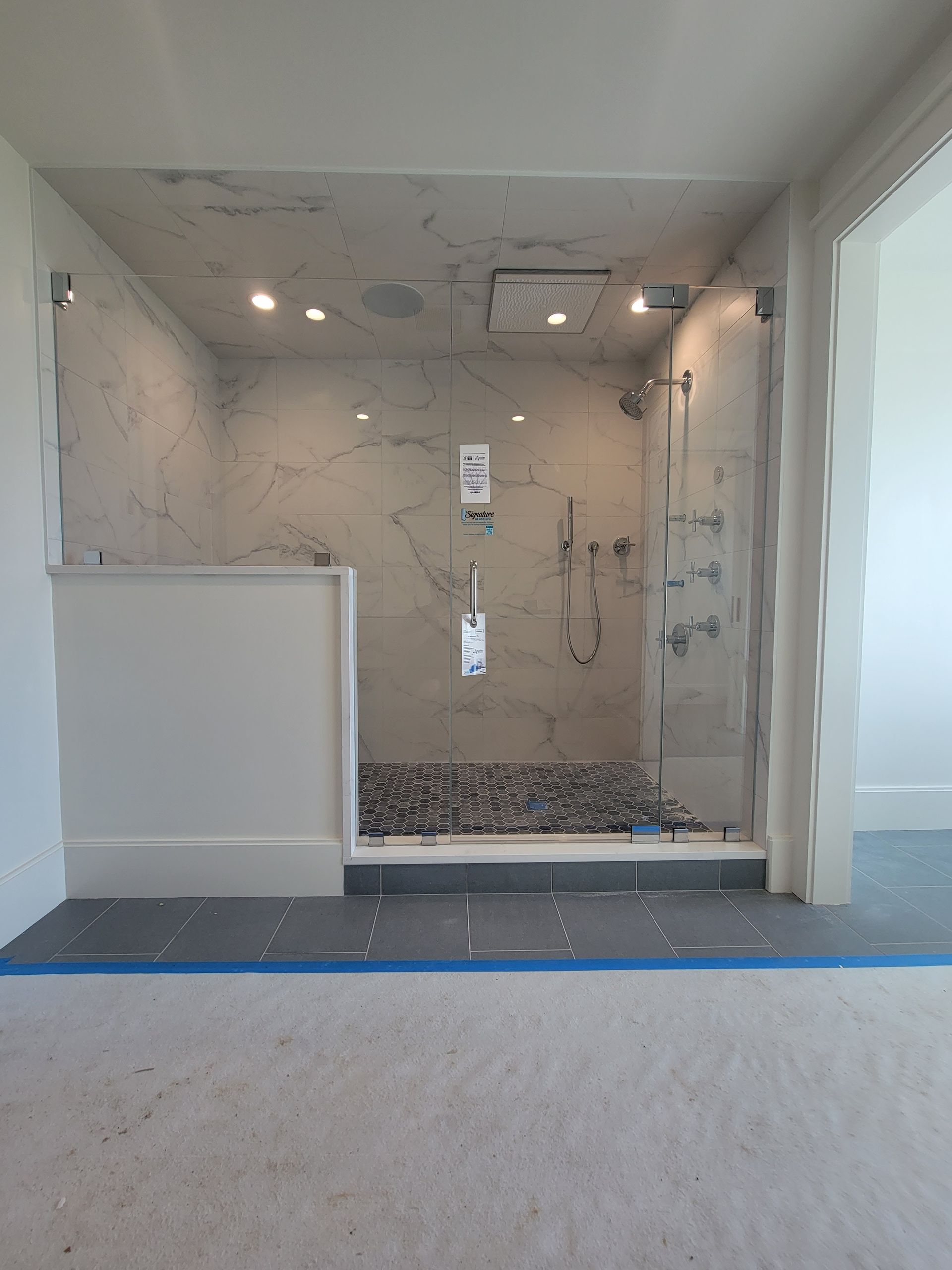 Frameless glass shower with marble walls and a pebble floor, in a newly constructed bathroom.