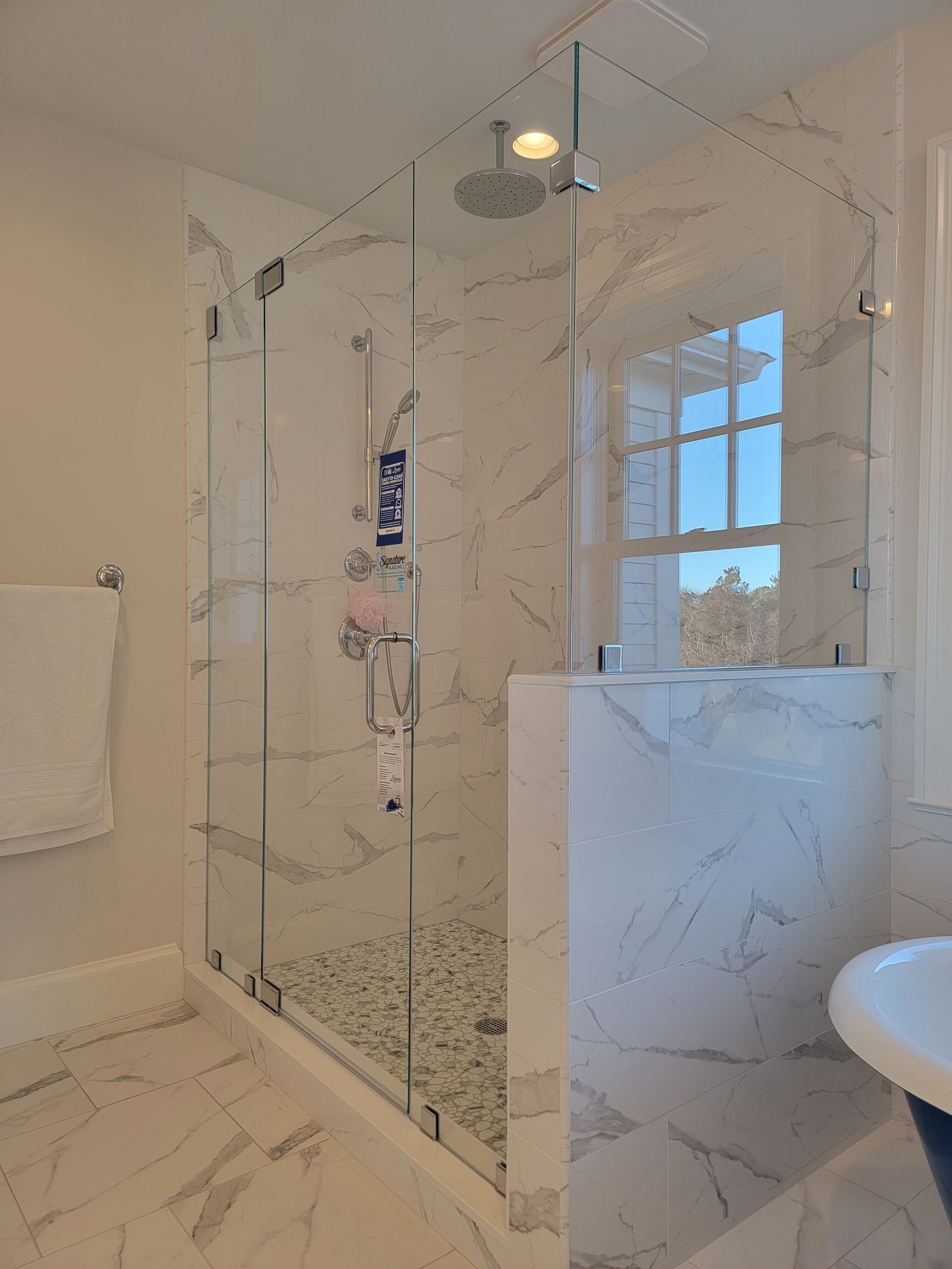 Marble-tiled shower with glass doors, a rain showerhead, and a window in the background.