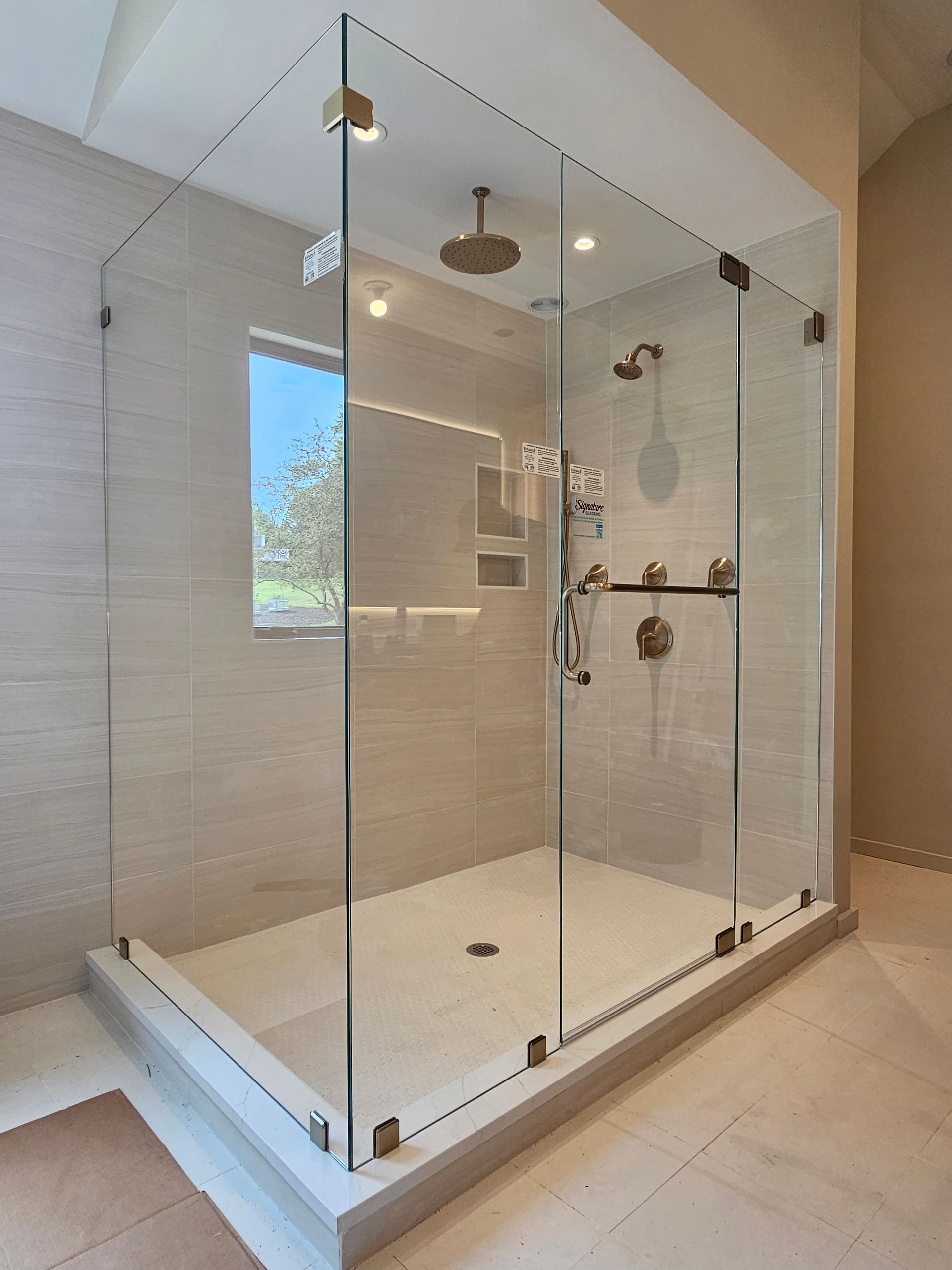 Glass shower enclosure with gold fixtures and light-colored tile.