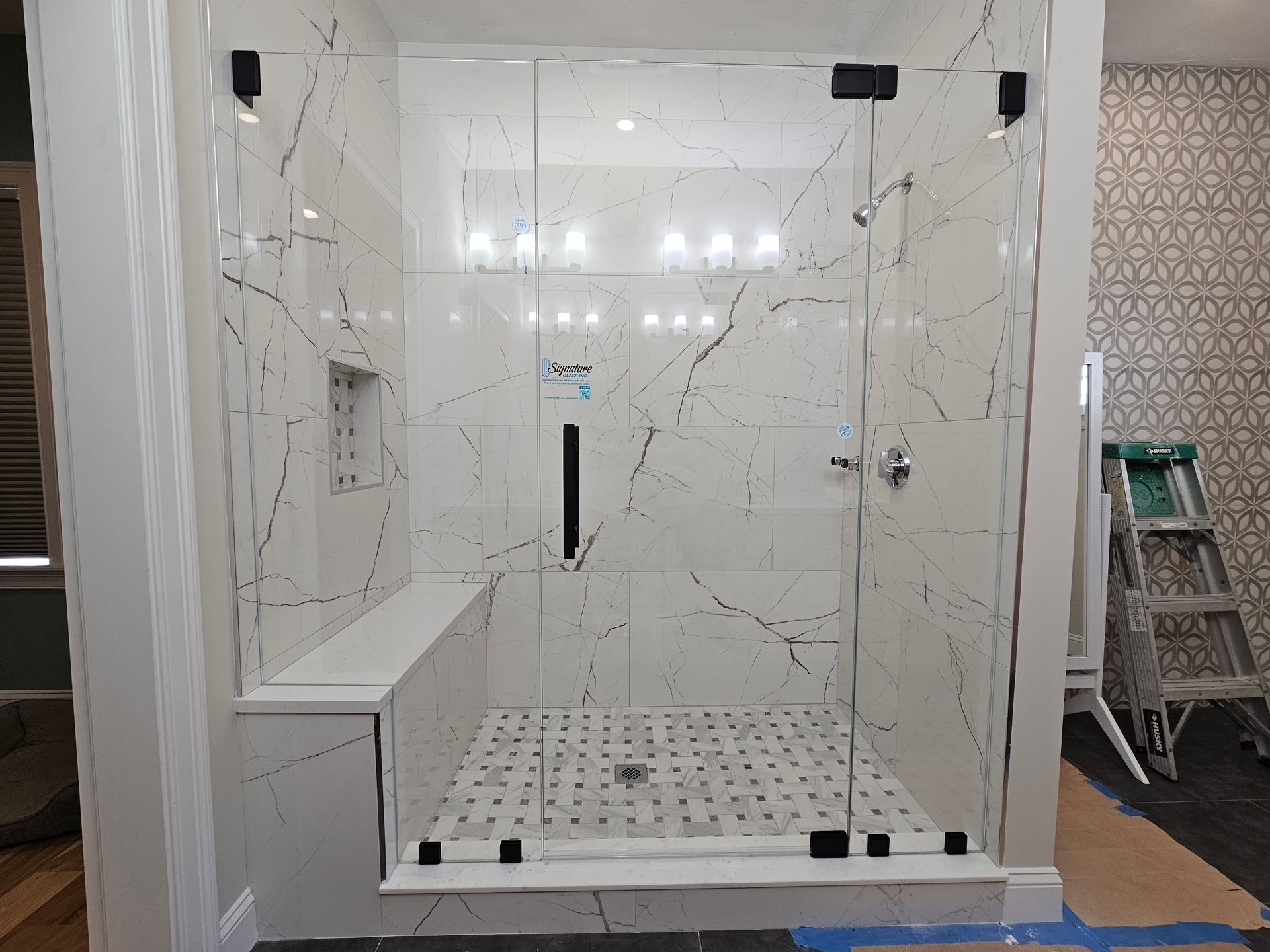 Modern walk-in shower with marble-look tile, glass doors, black hardware, and built-in bench.