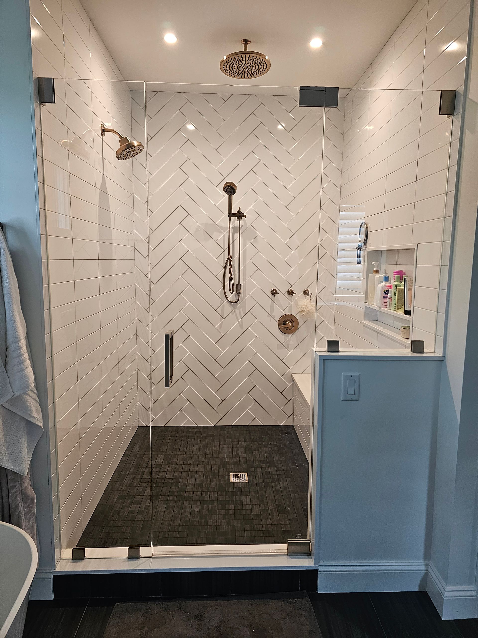 Modern shower with glass door and black stone floor. White tile walls with herringbone pattern.