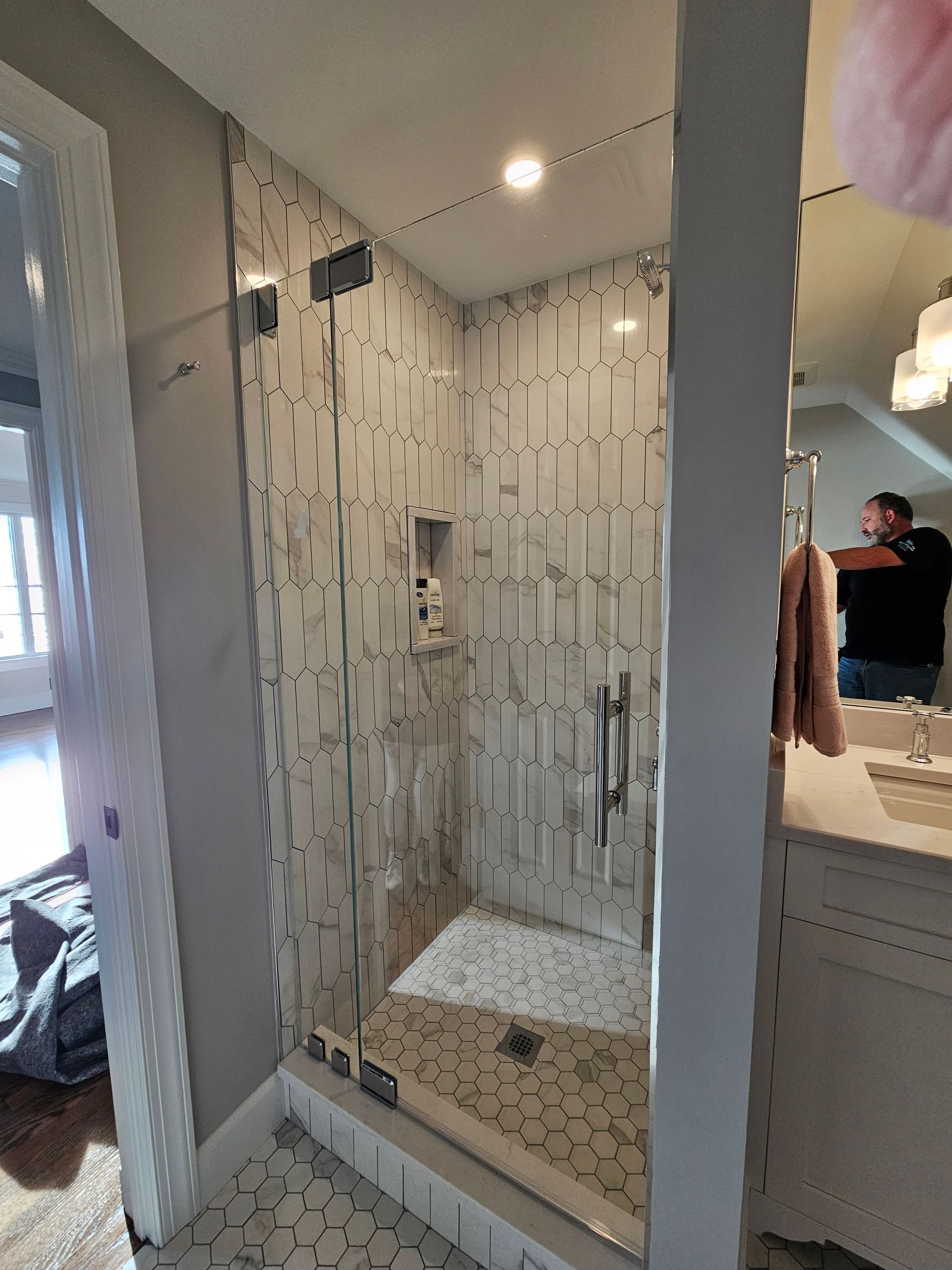 Glass shower with patterned tile, chrome fixtures, and a person reflected in the mirror.