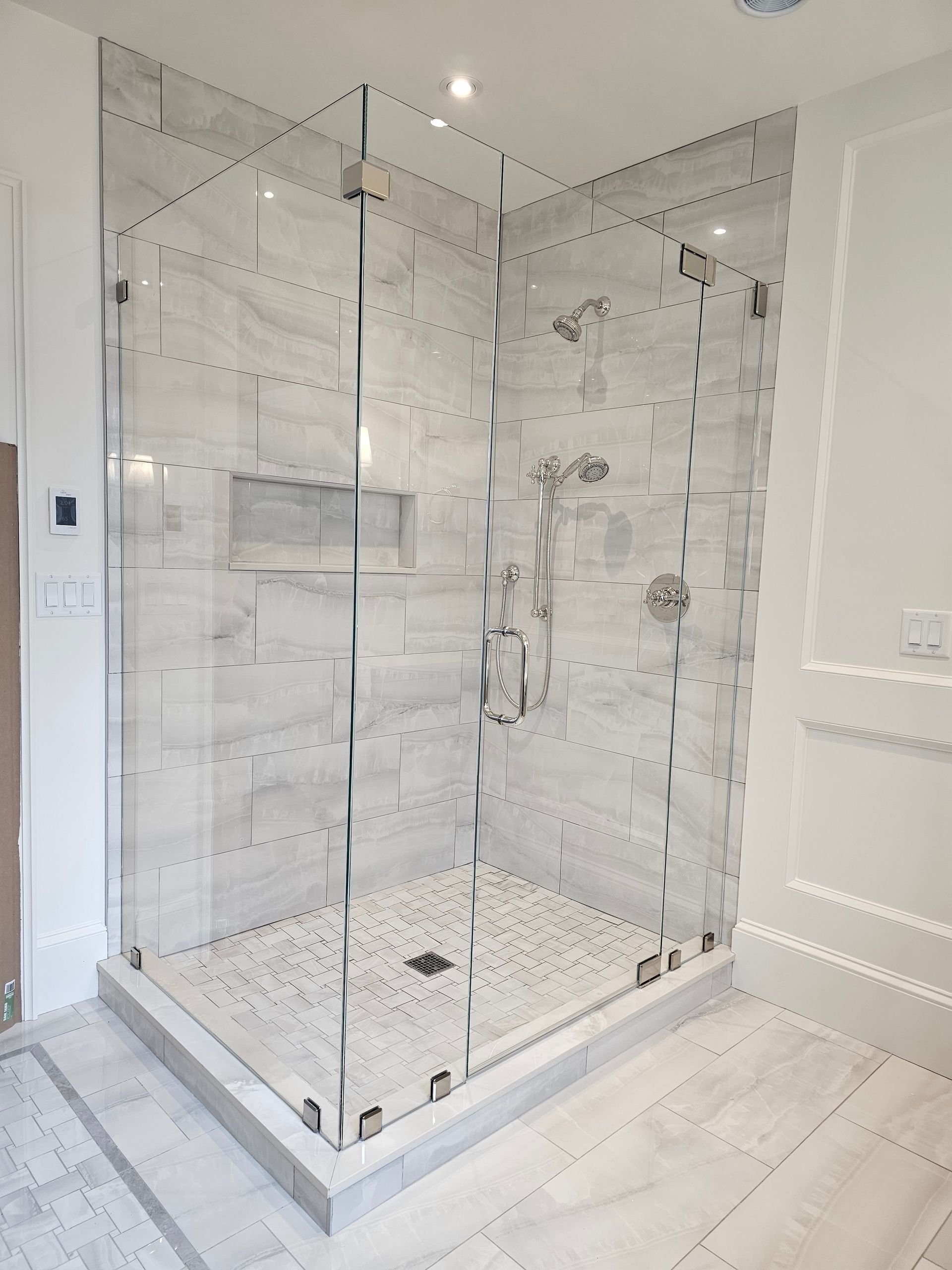 Glass shower enclosure with white tile walls and pebbled floor. Chrome fixtures.