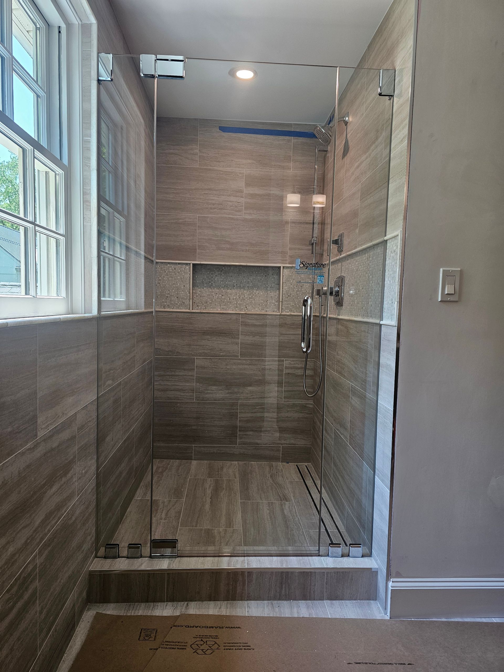Shower with glass doors and brown tile. Window on left.