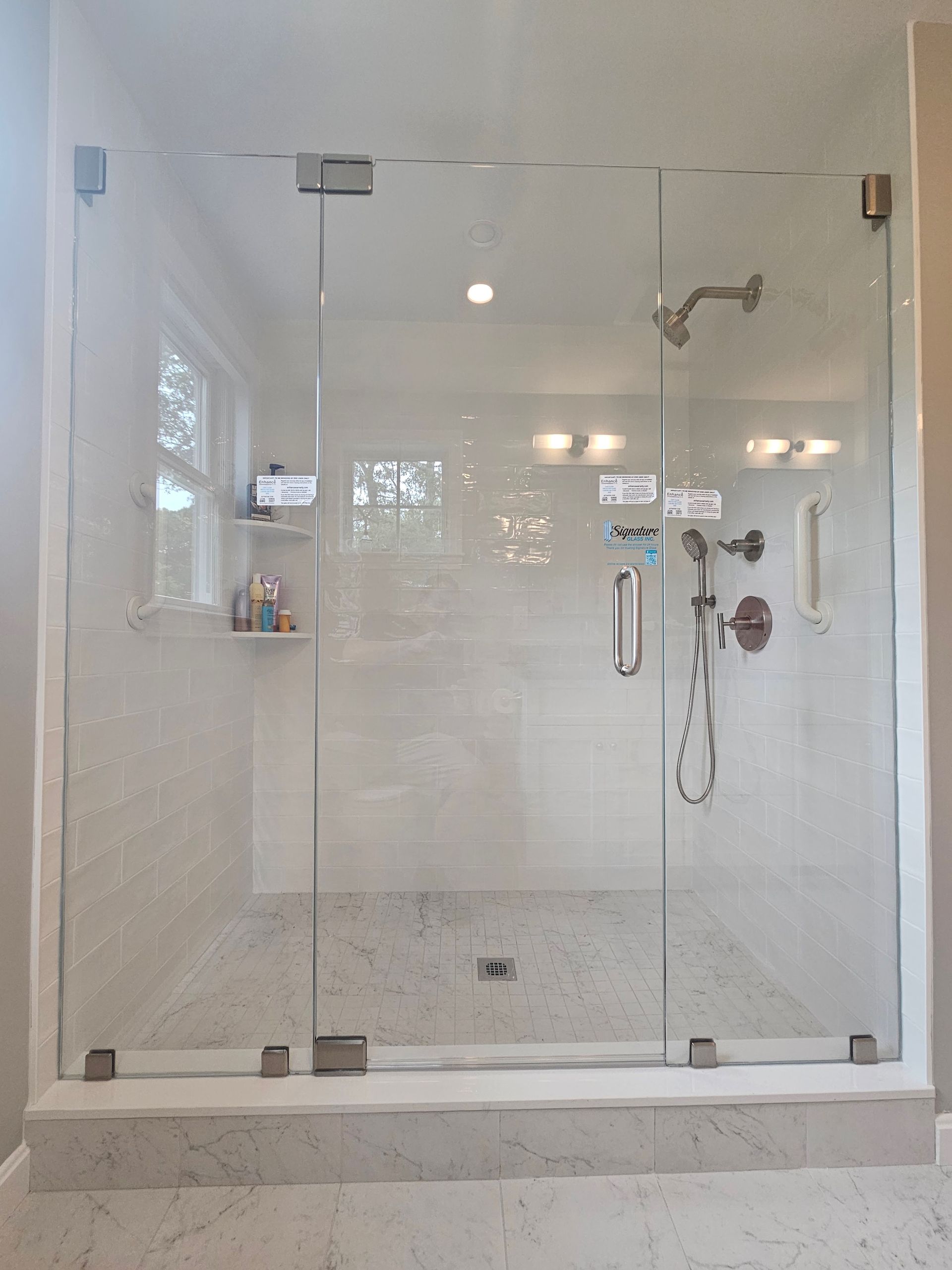 Glass-walled shower with two doors, silver fixtures, and white tiled interior.