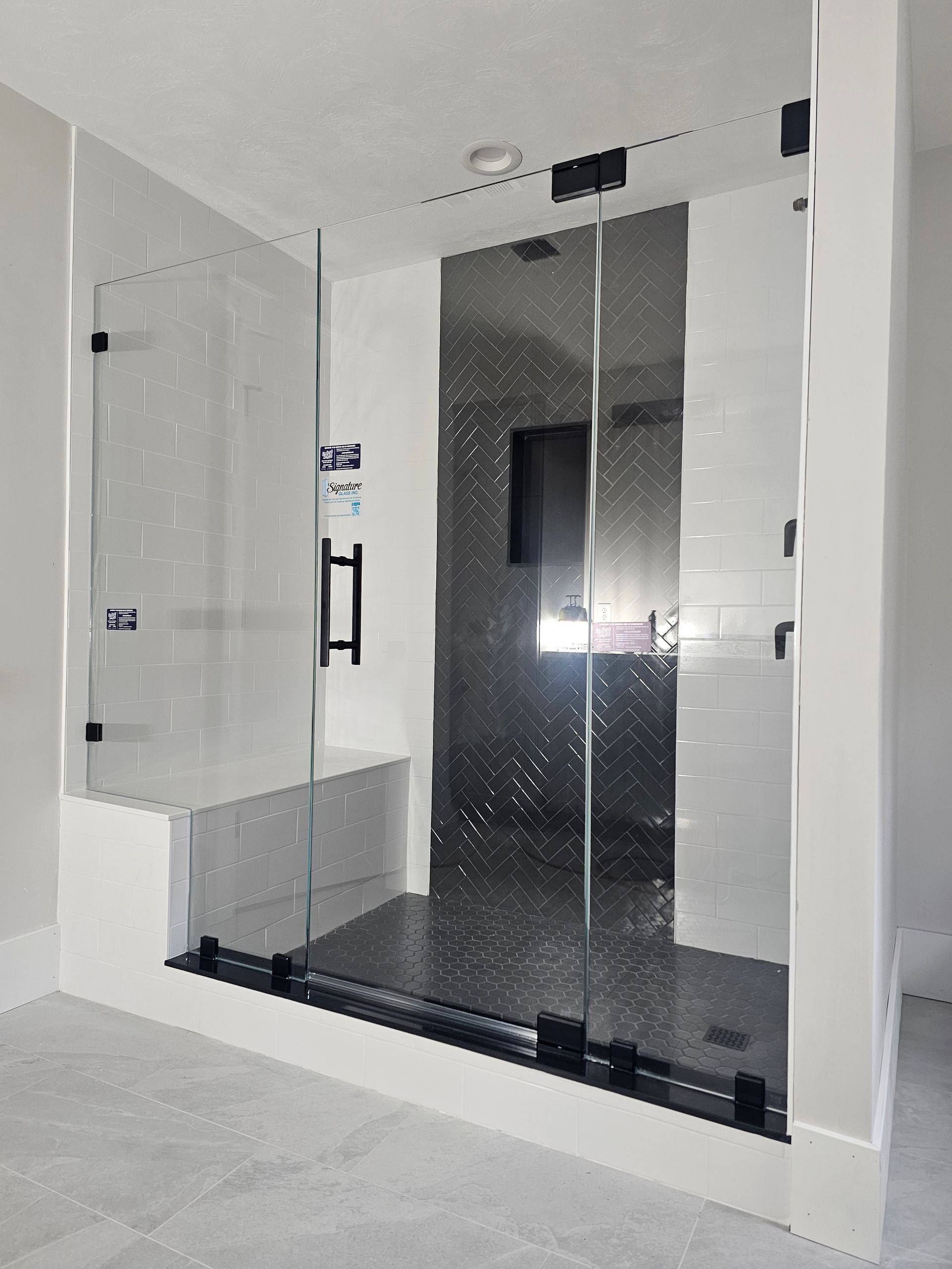 Glass-walled walk-in shower with black hardware, bench, and textured gray back wall.