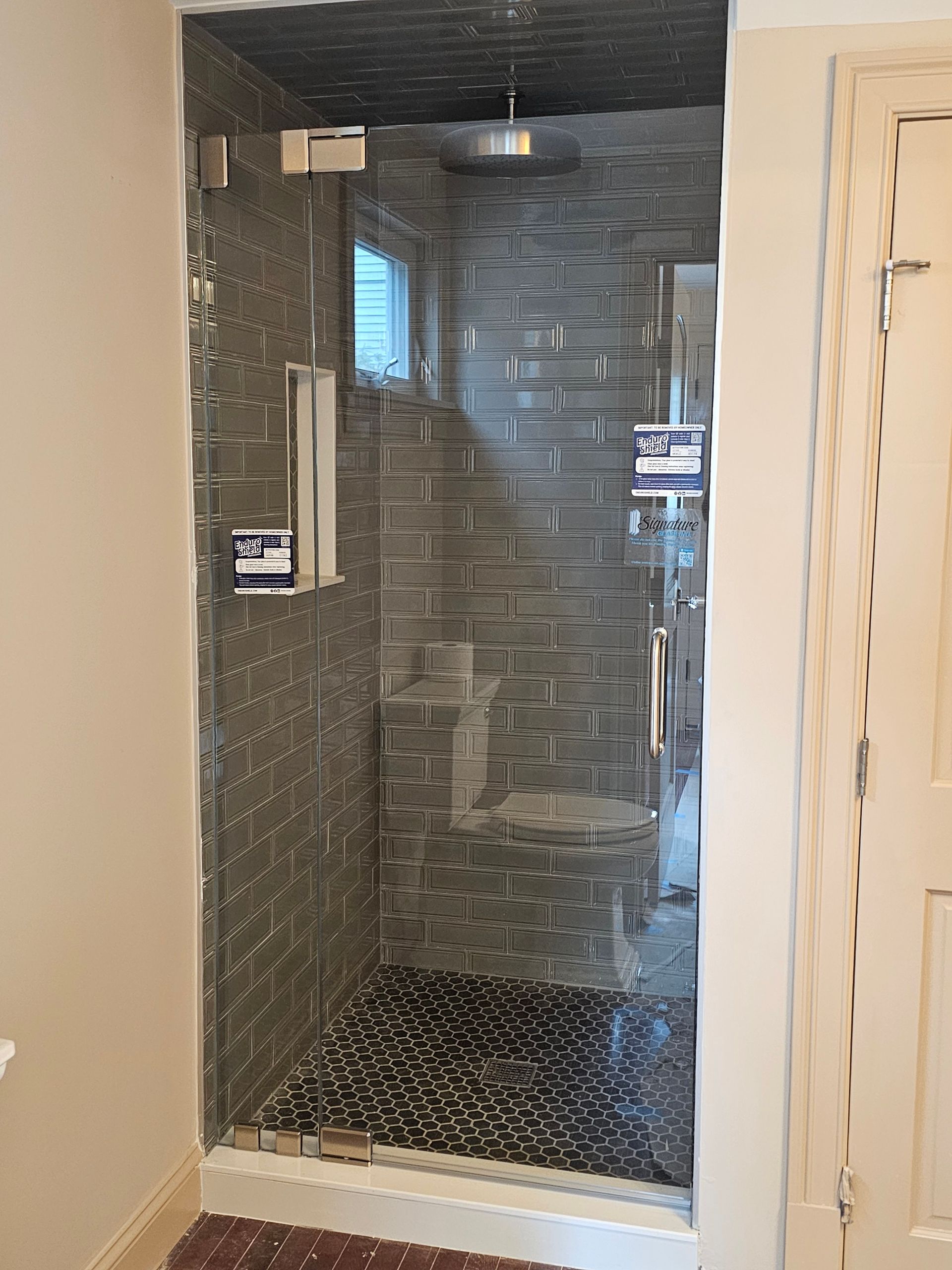 Glass shower enclosure with gray tiled walls and dark stone floor.
