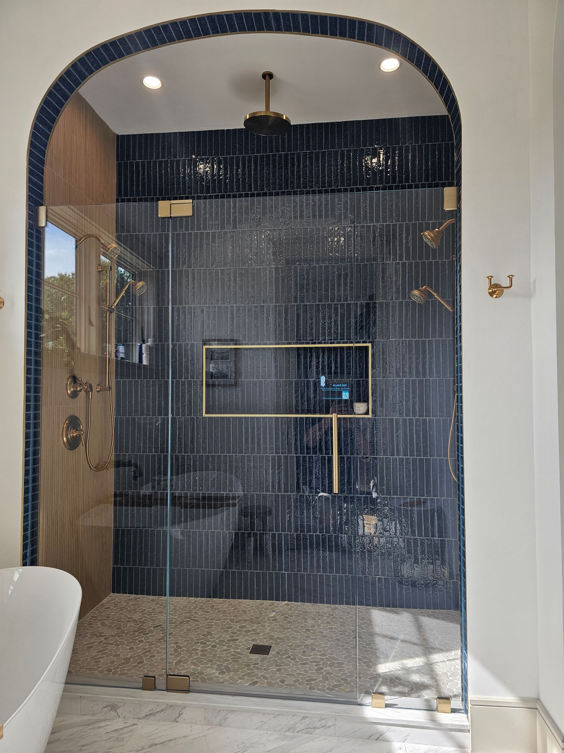 Luxurious navy blue tiled shower with gold fixtures, glass doors, and pebble floor.
