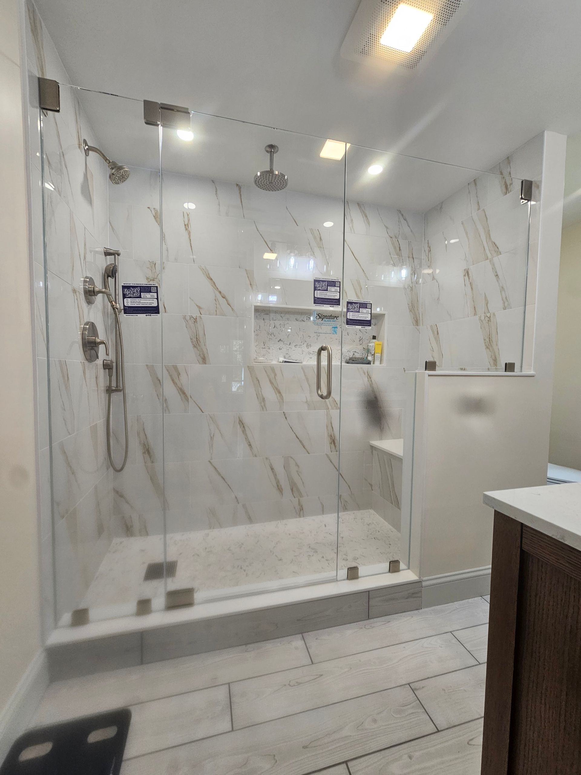 A modern, tiled shower with glass doors, multiple shower heads, and recessed shelving.