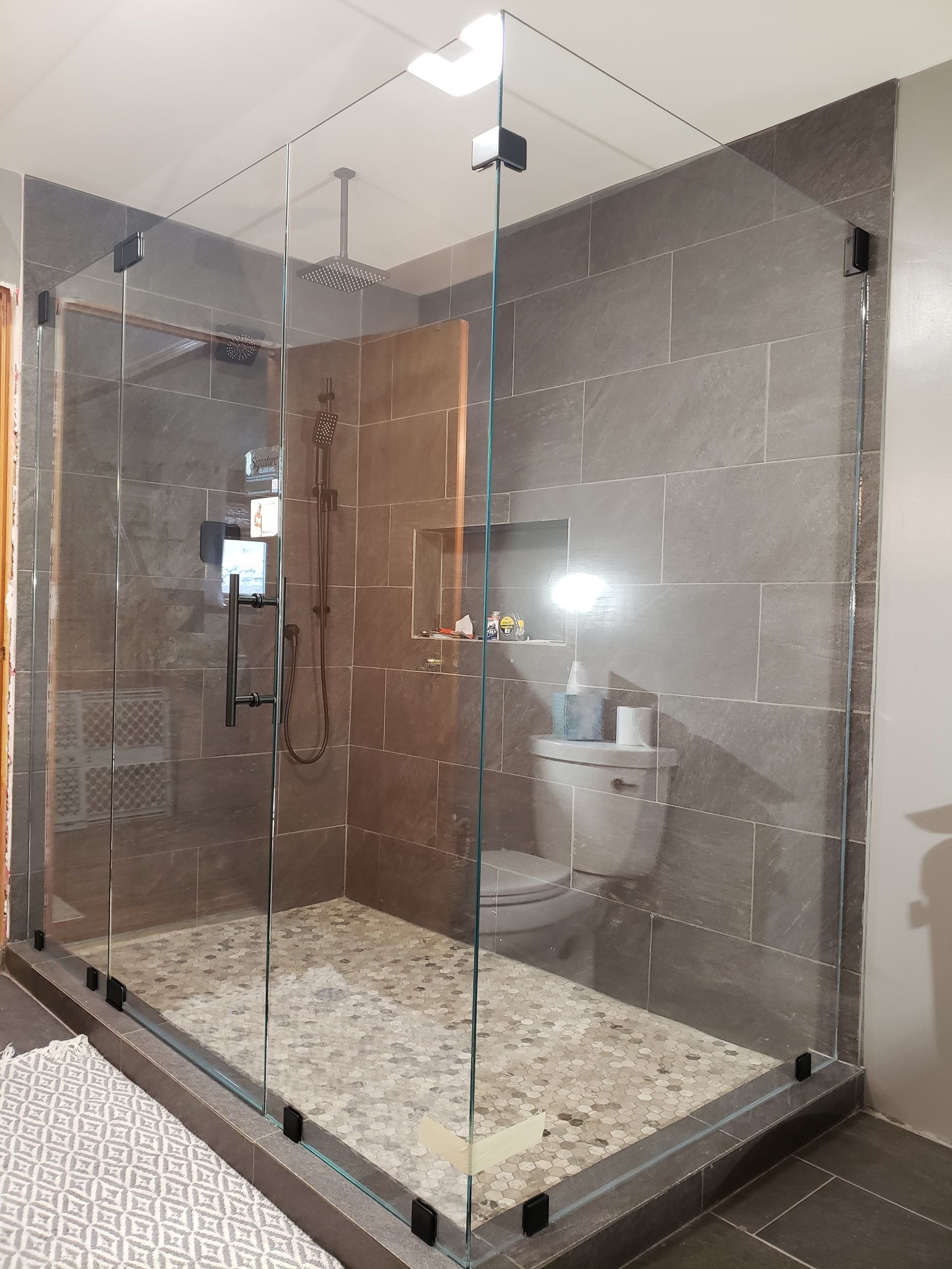 Glass shower with pebble floor and gray tiled walls, includes a toilet.