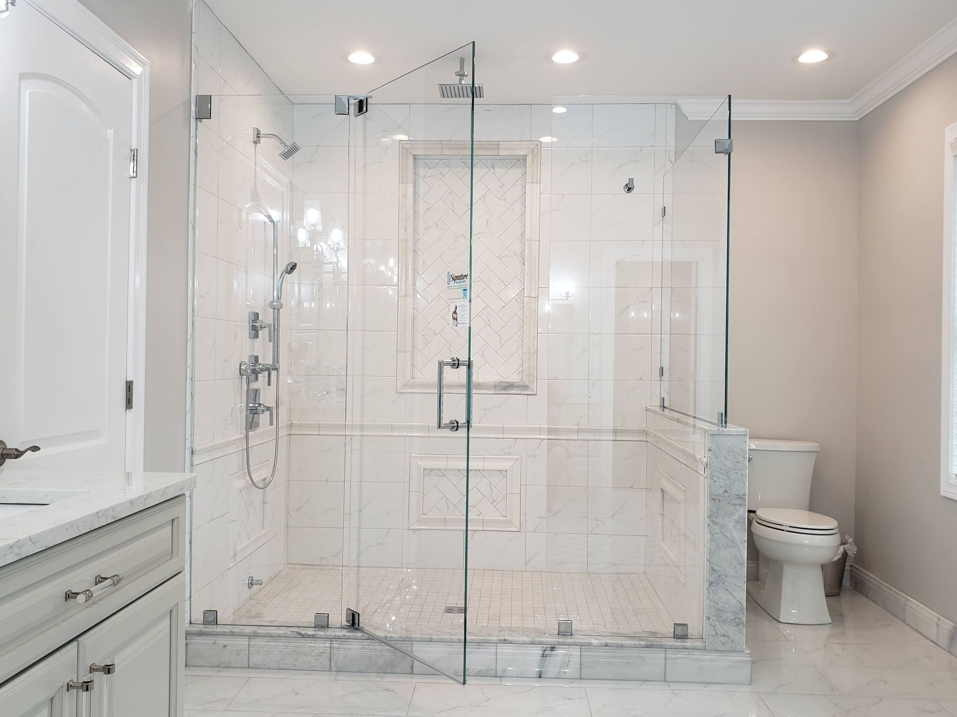 Spacious white tiled bathroom with a large glass shower enclosure, toilet, and vanity.