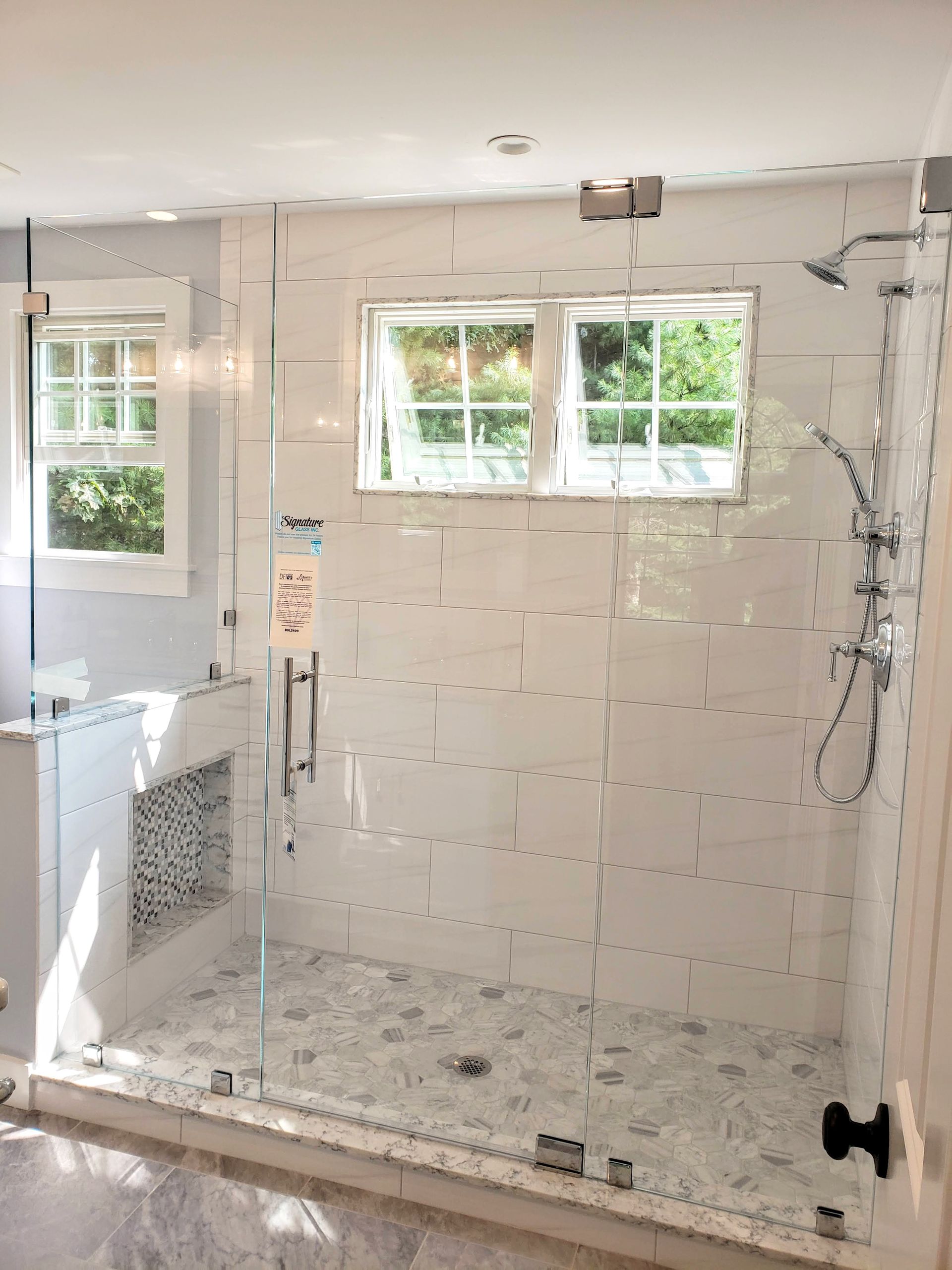 Glass shower with white tiled walls, a small window, and mosaic floor.