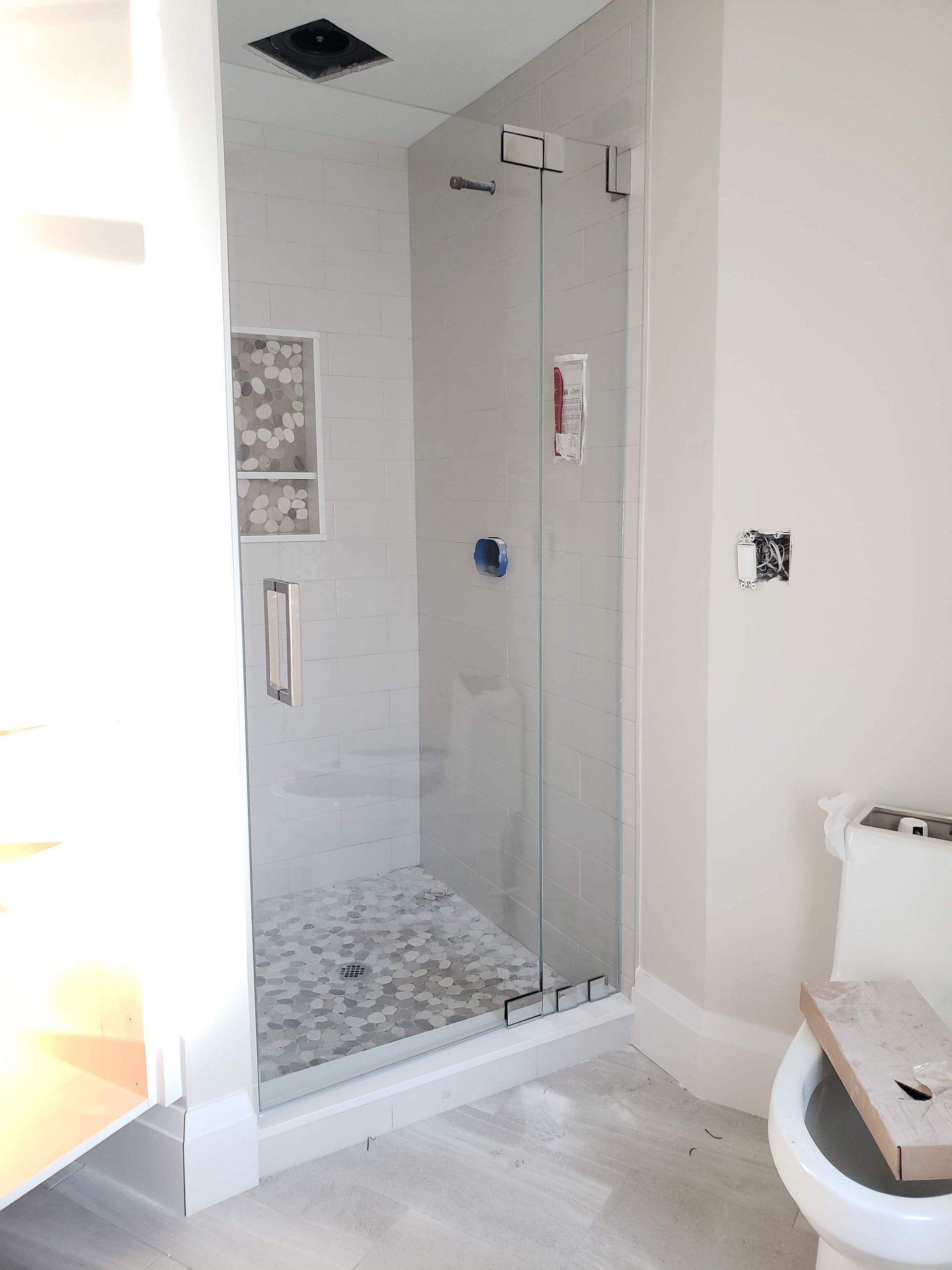 Shower with glass door, gray tile, pebble floor, and white walls.