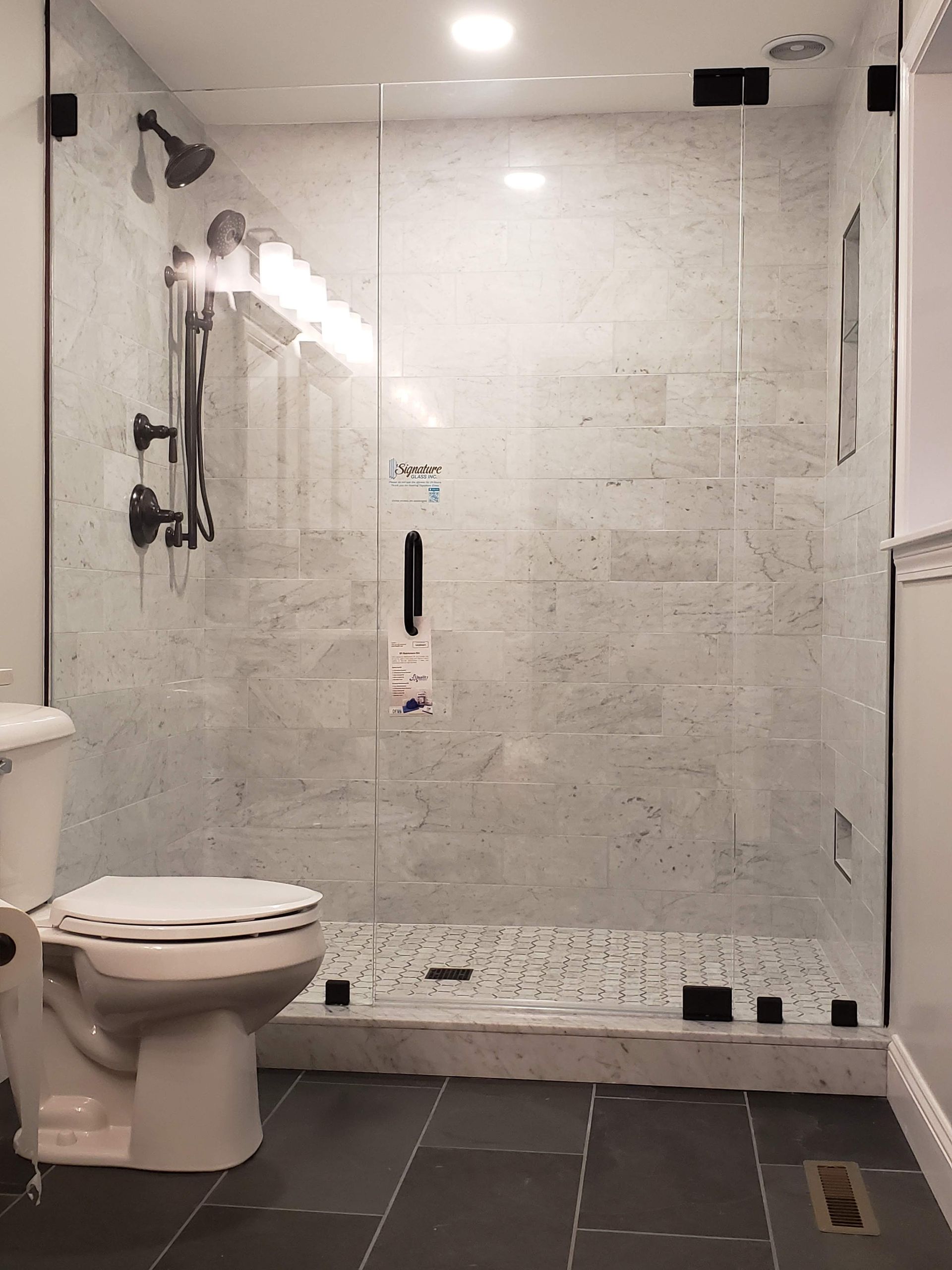 Modern bathroom with glass shower enclosure, gray tiled walls, black fixtures, and toilet.