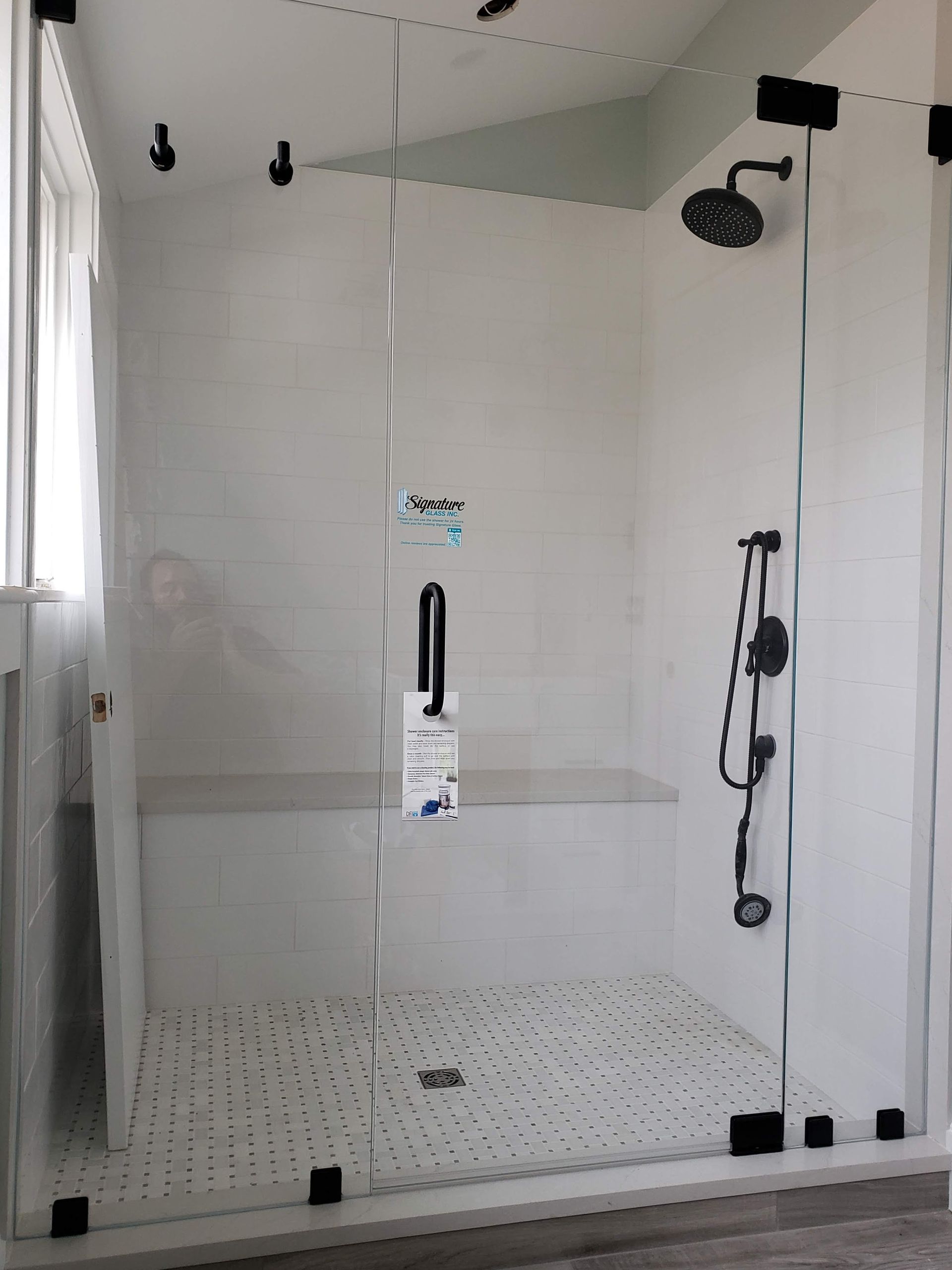 Modern white shower with glass walls, black hardware, and a built-in bench.