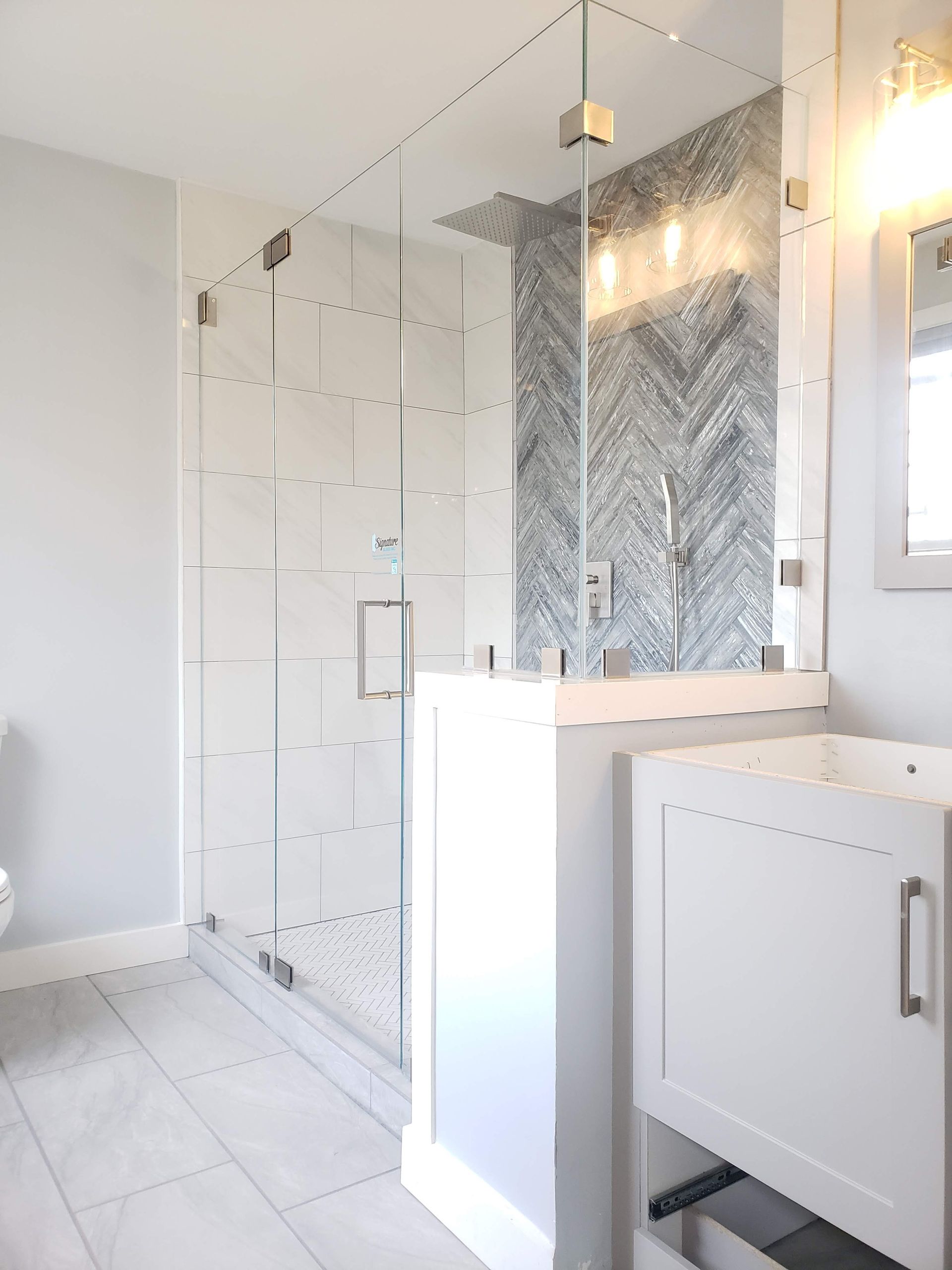 Modern bathroom with glass shower, white vanity, and gray tile accent wall.