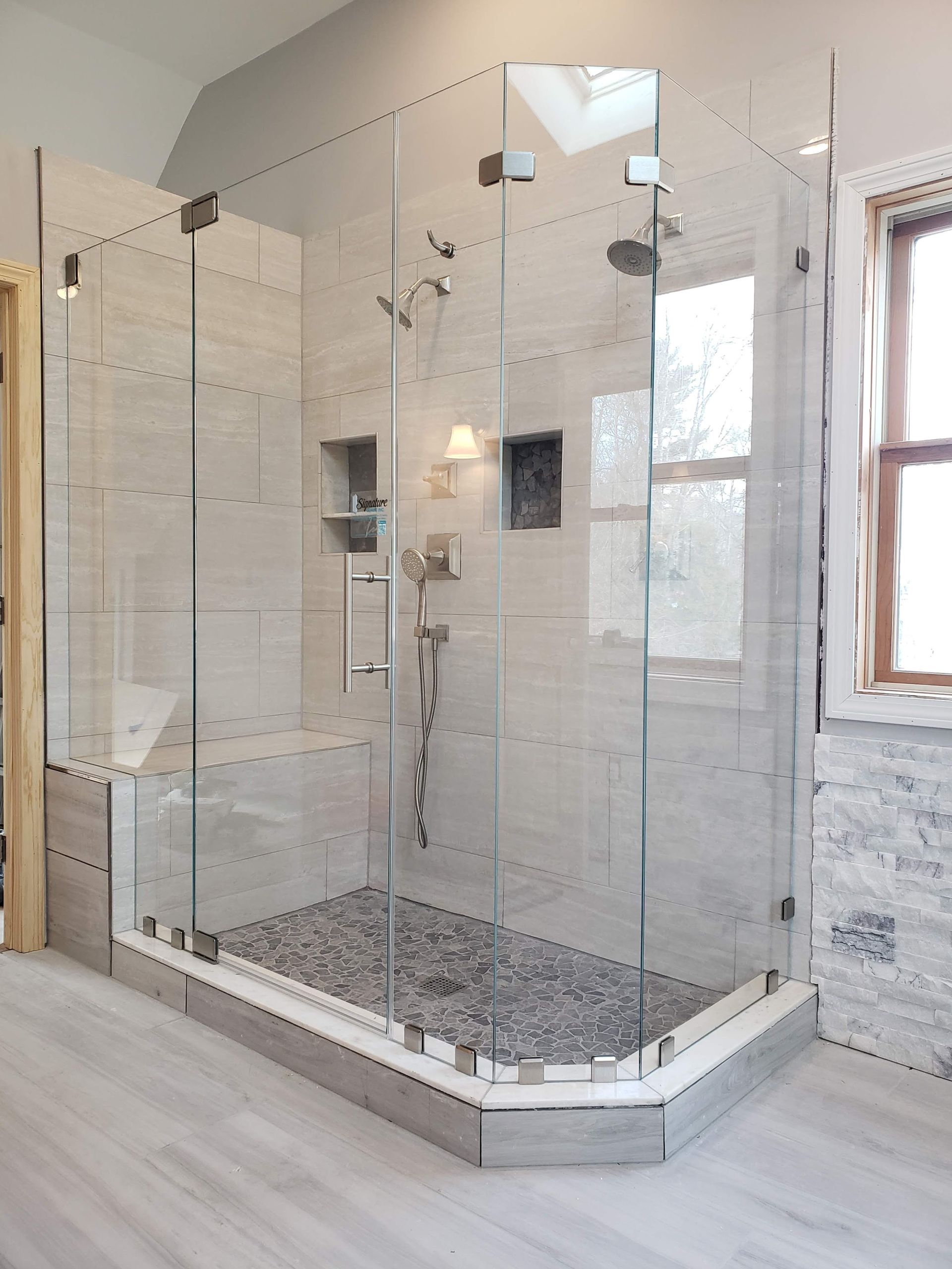 Modern glass shower enclosure with pebble floor and stone tile walls.