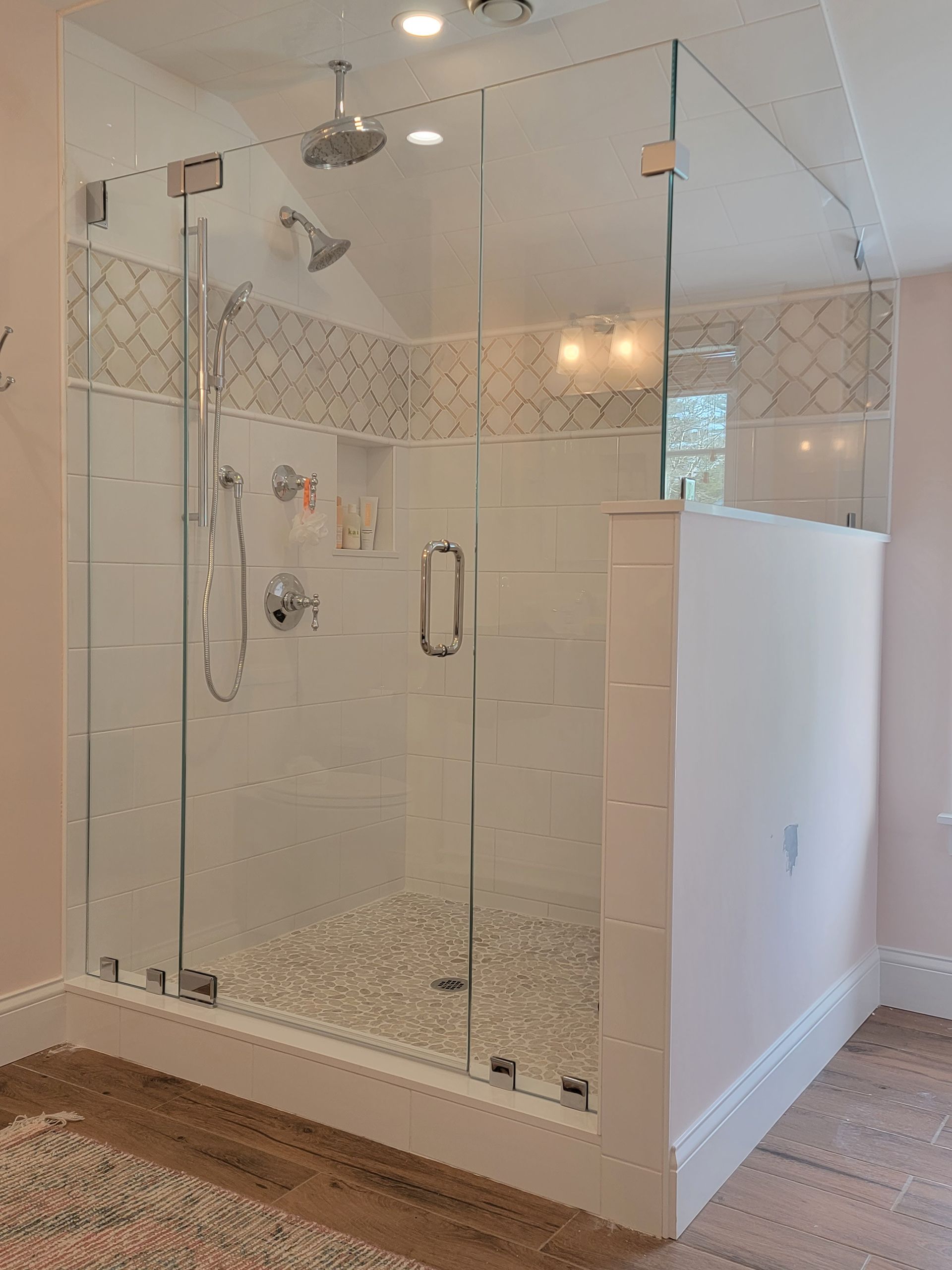 Glass-walled shower with white tile and pebble floor. Pink walls, chrome fixtures.