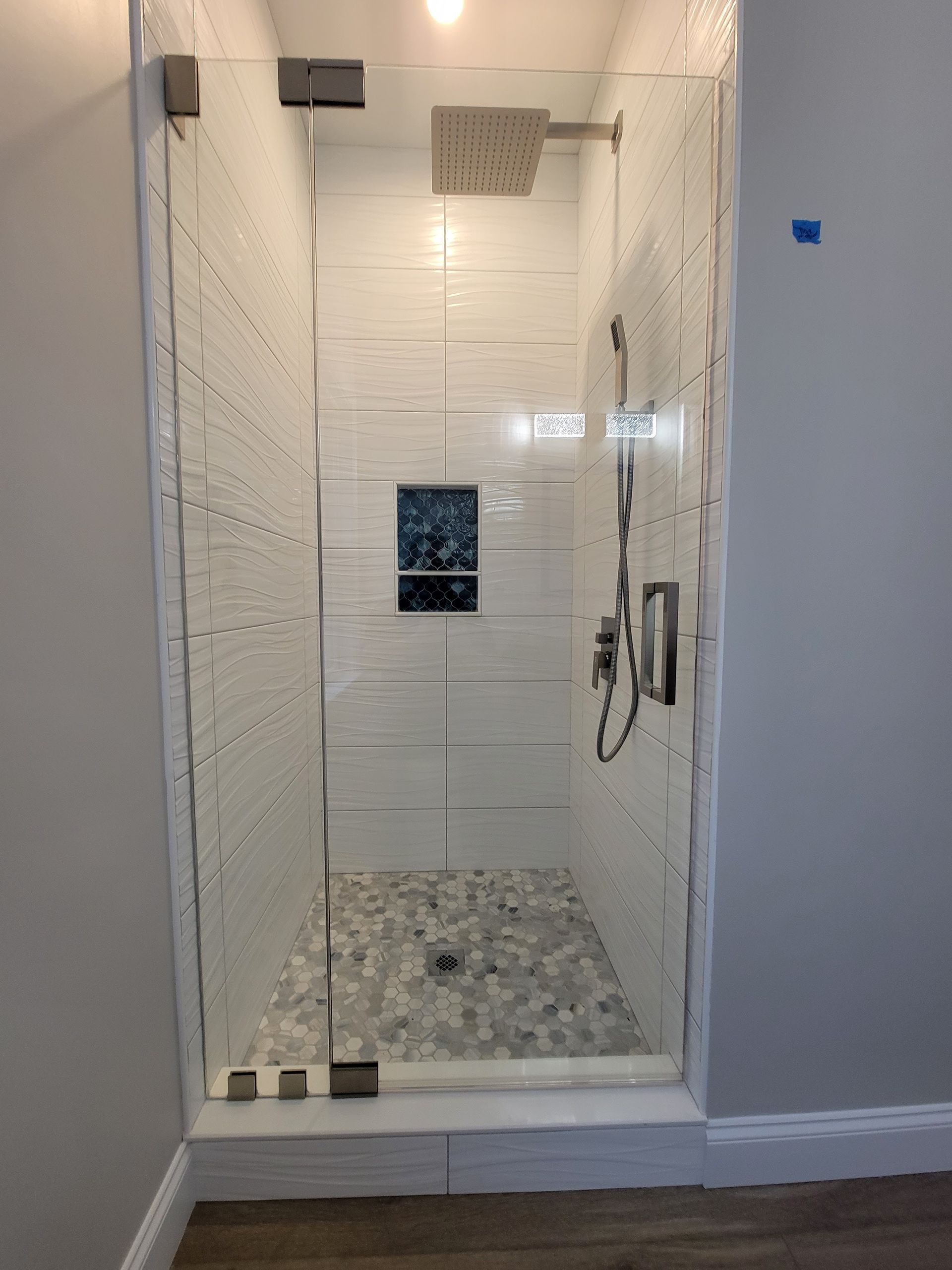 Glass shower with white textured tile walls, gray pebble floor, and stainless steel fixtures.