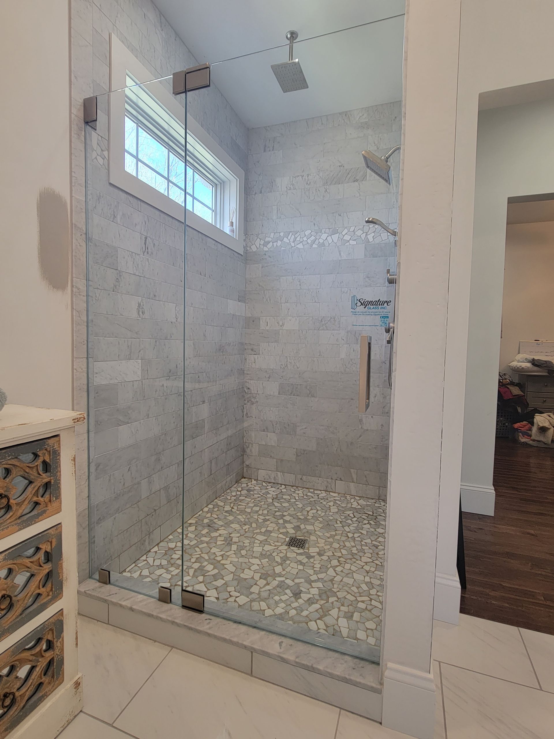 Glass shower enclosure with gray tile walls and pebble floor.