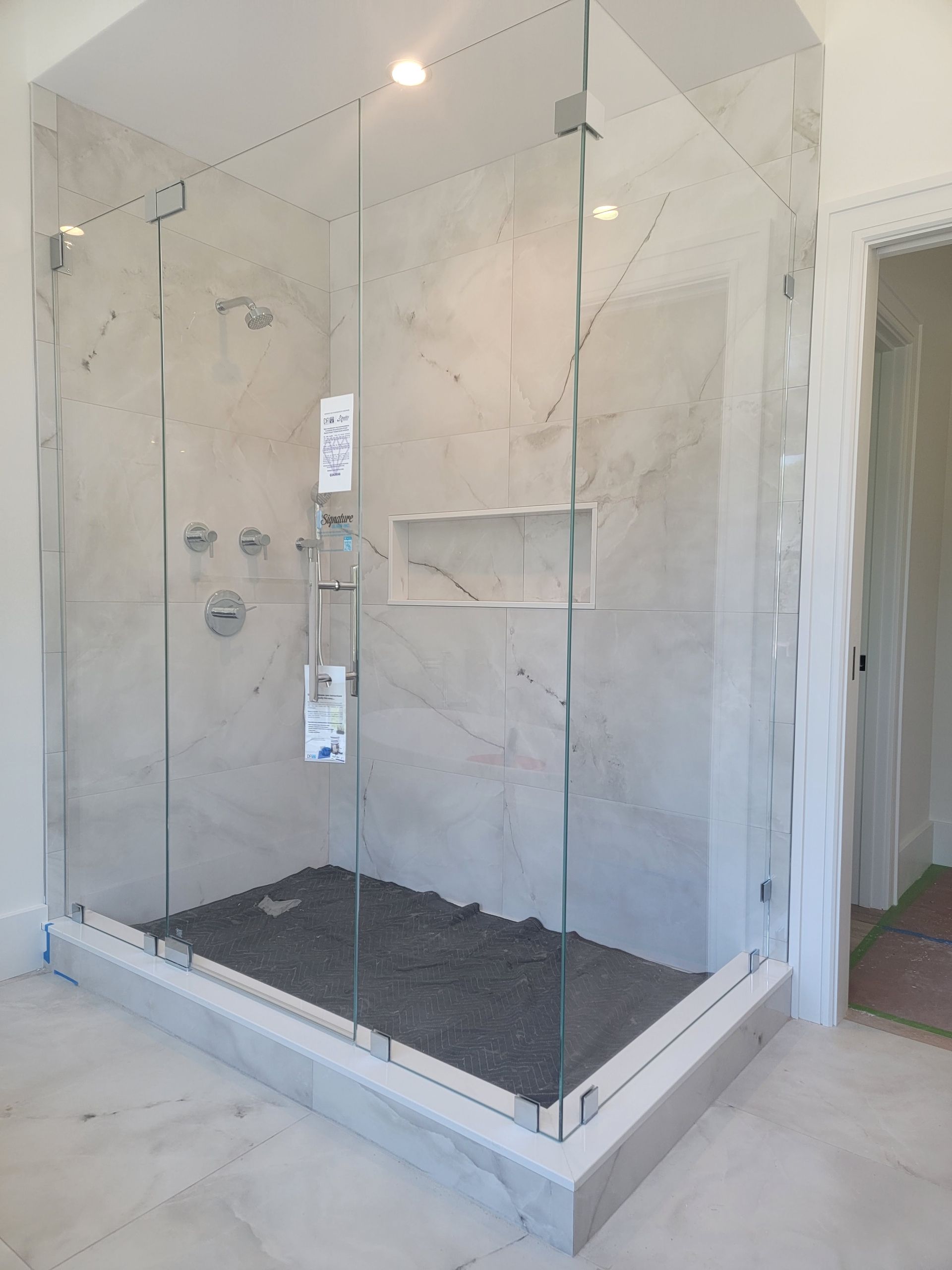 Glass shower enclosure with gray stone tile interior and black pebble floor.