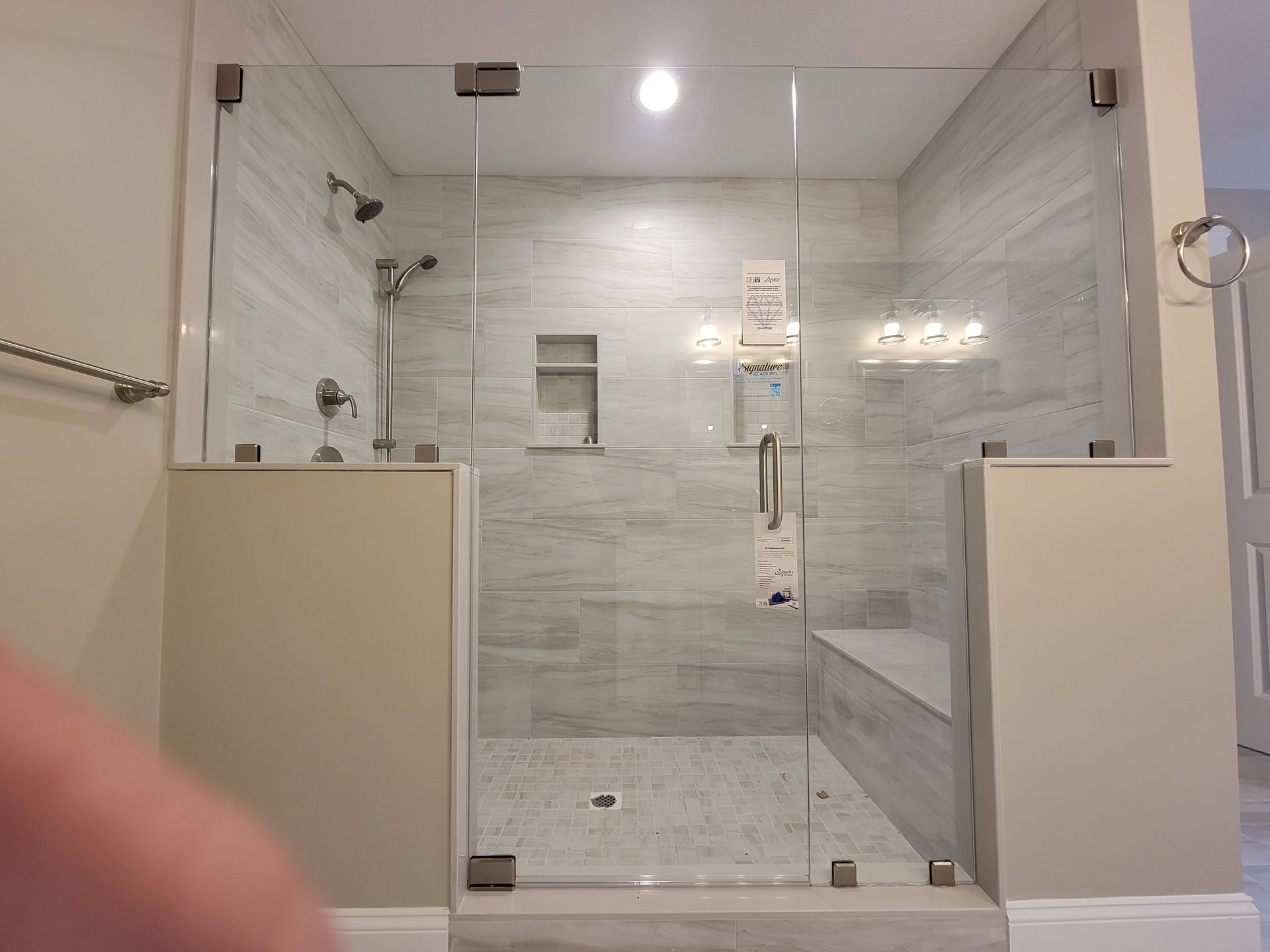Glass-enclosed shower with tiled walls and a bench seat. Polished hardware. Neutral tones.