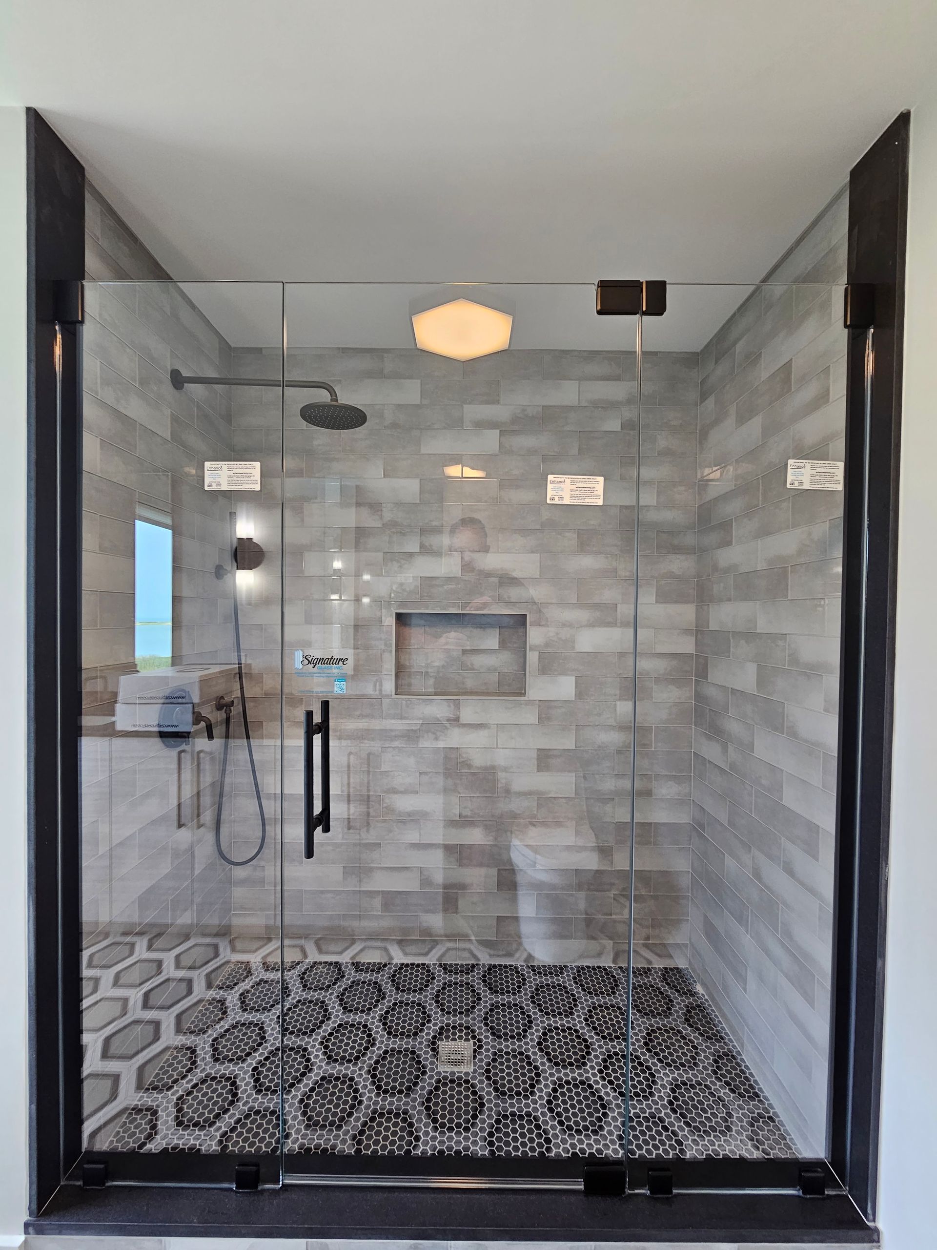 Modern walk-in shower with gray tiled walls and patterned floor. Black door frame and fixtures.