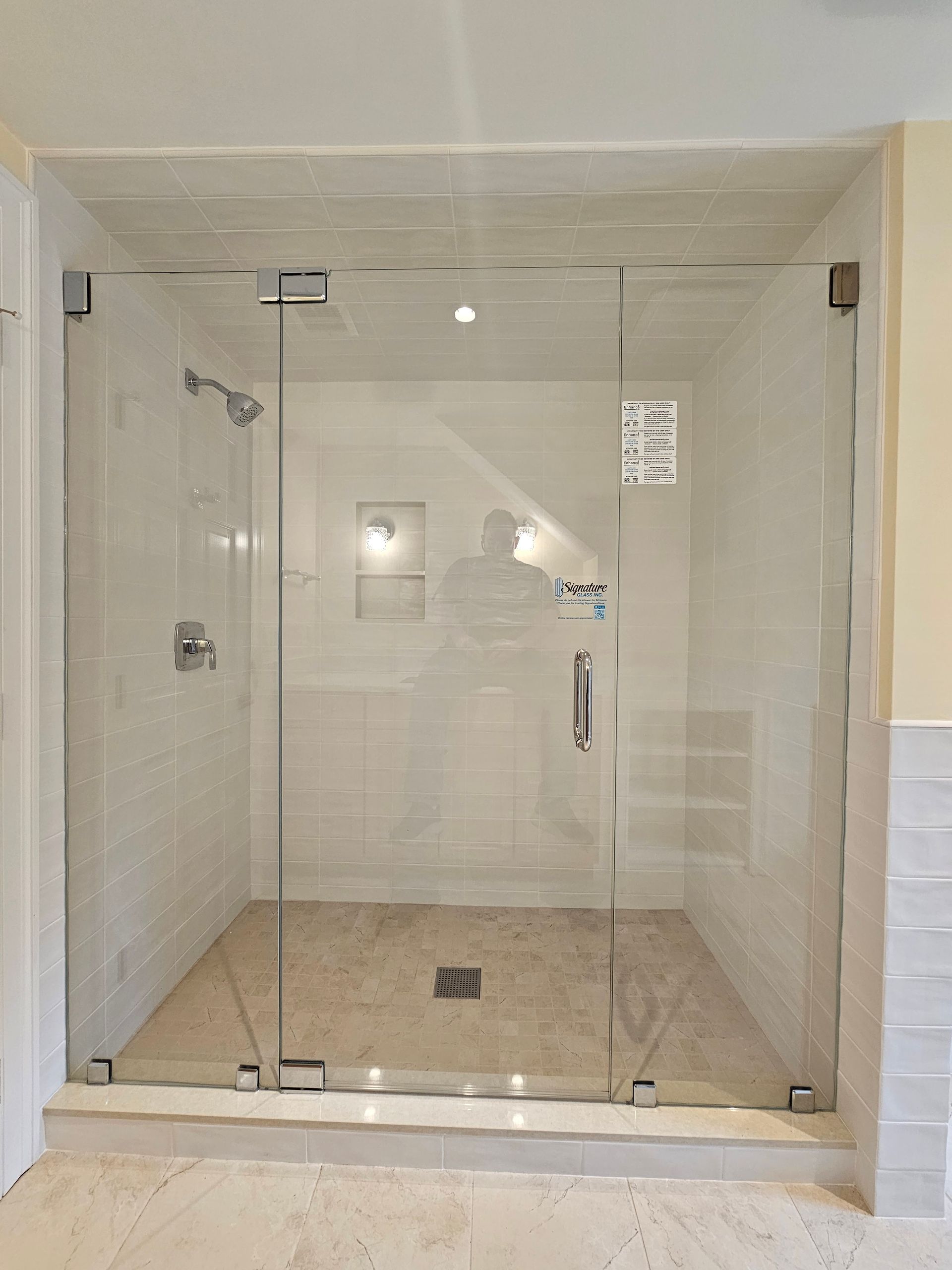 Glass shower enclosure in a bathroom with white tile walls and a stone floor.