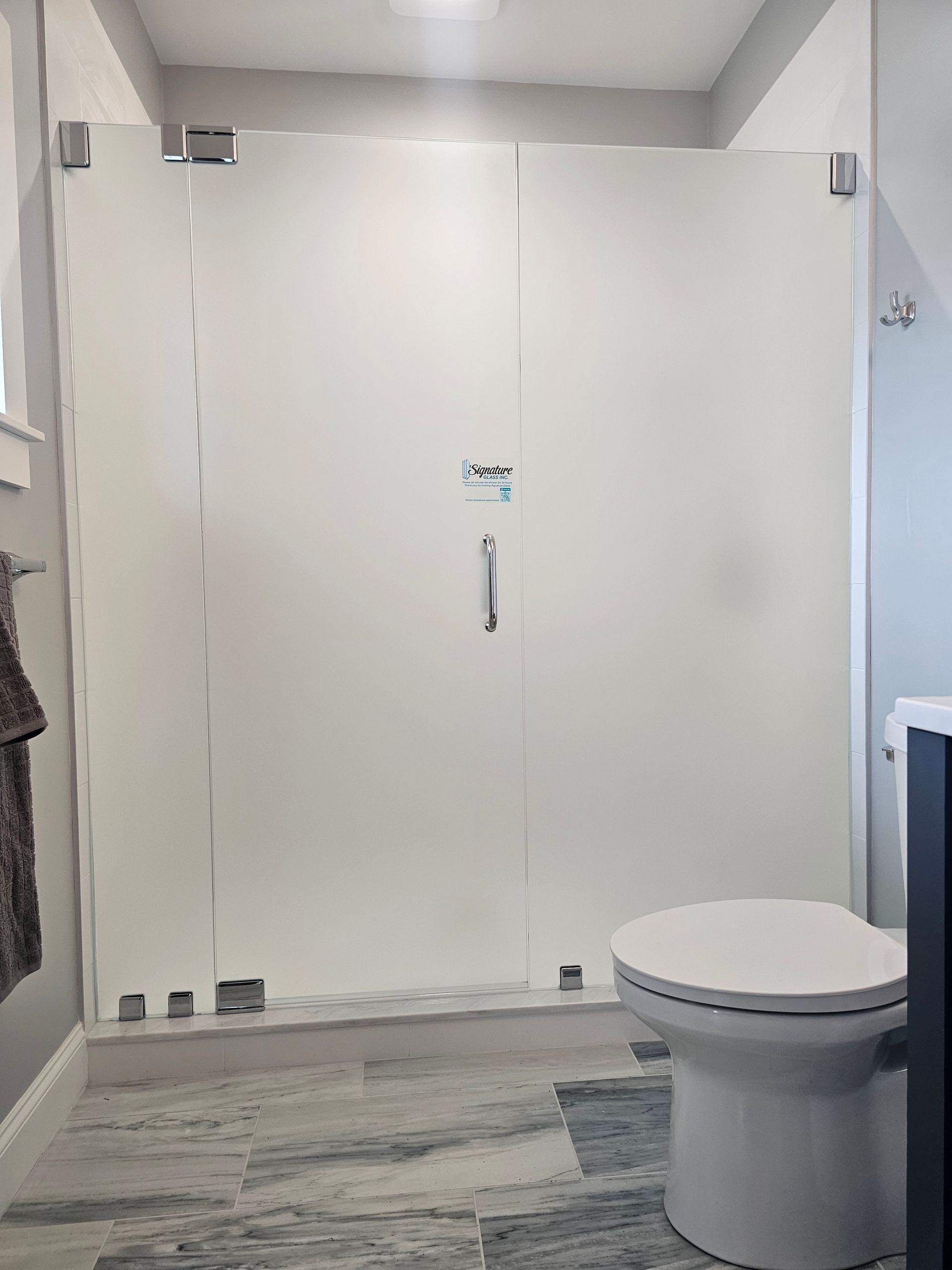 Bathroom with frosted glass shower doors, white toilet, and blue-gray tile floor.