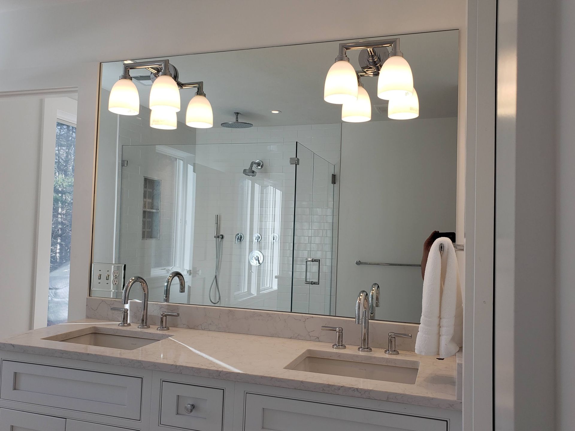 Bathroom with a large mirror, double sink vanity, and glass-enclosed shower. White fixtures and trim.