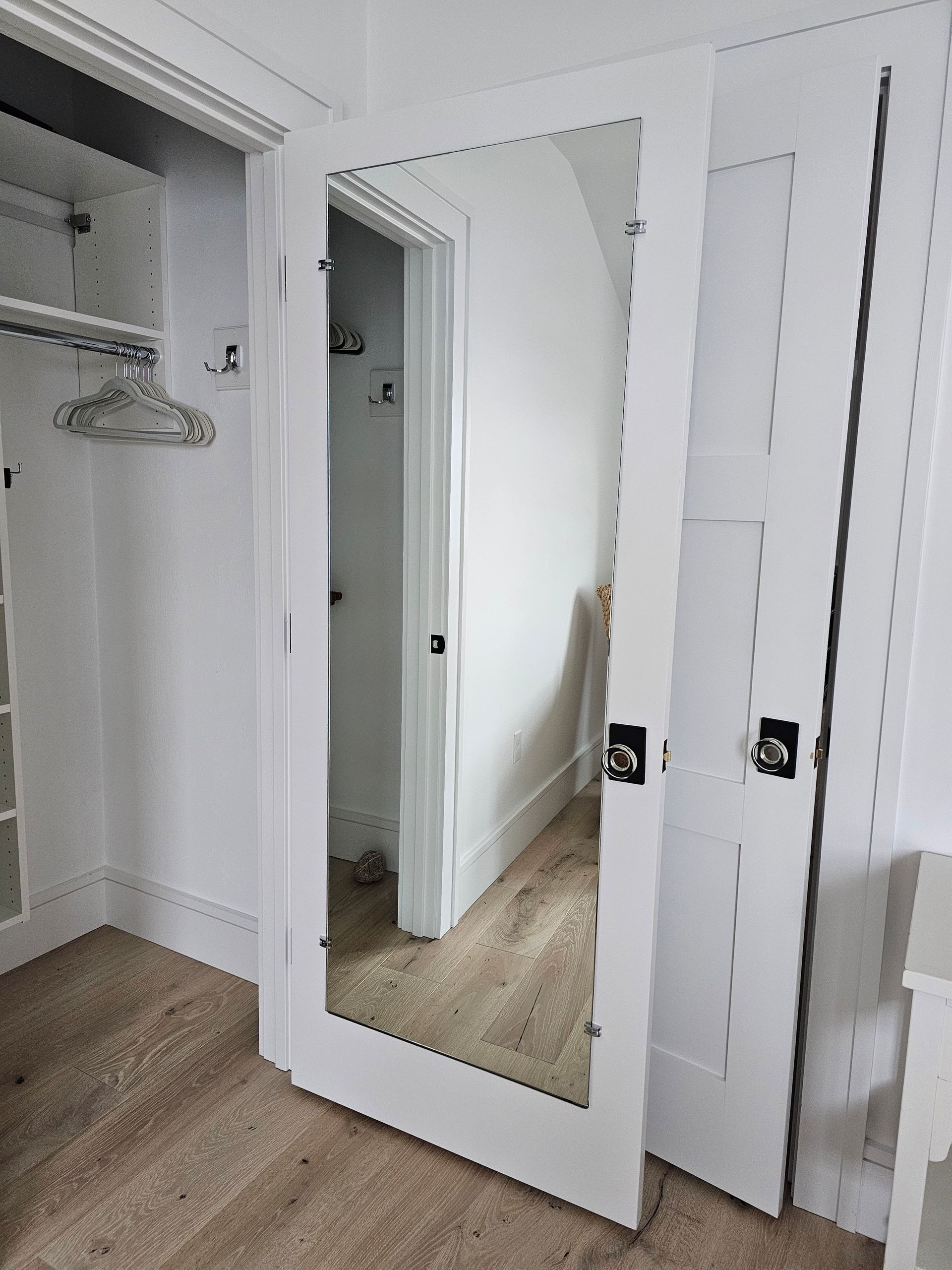 White framed mirror door, partially open revealing a closet with a clothes rack. The floor is light brown.