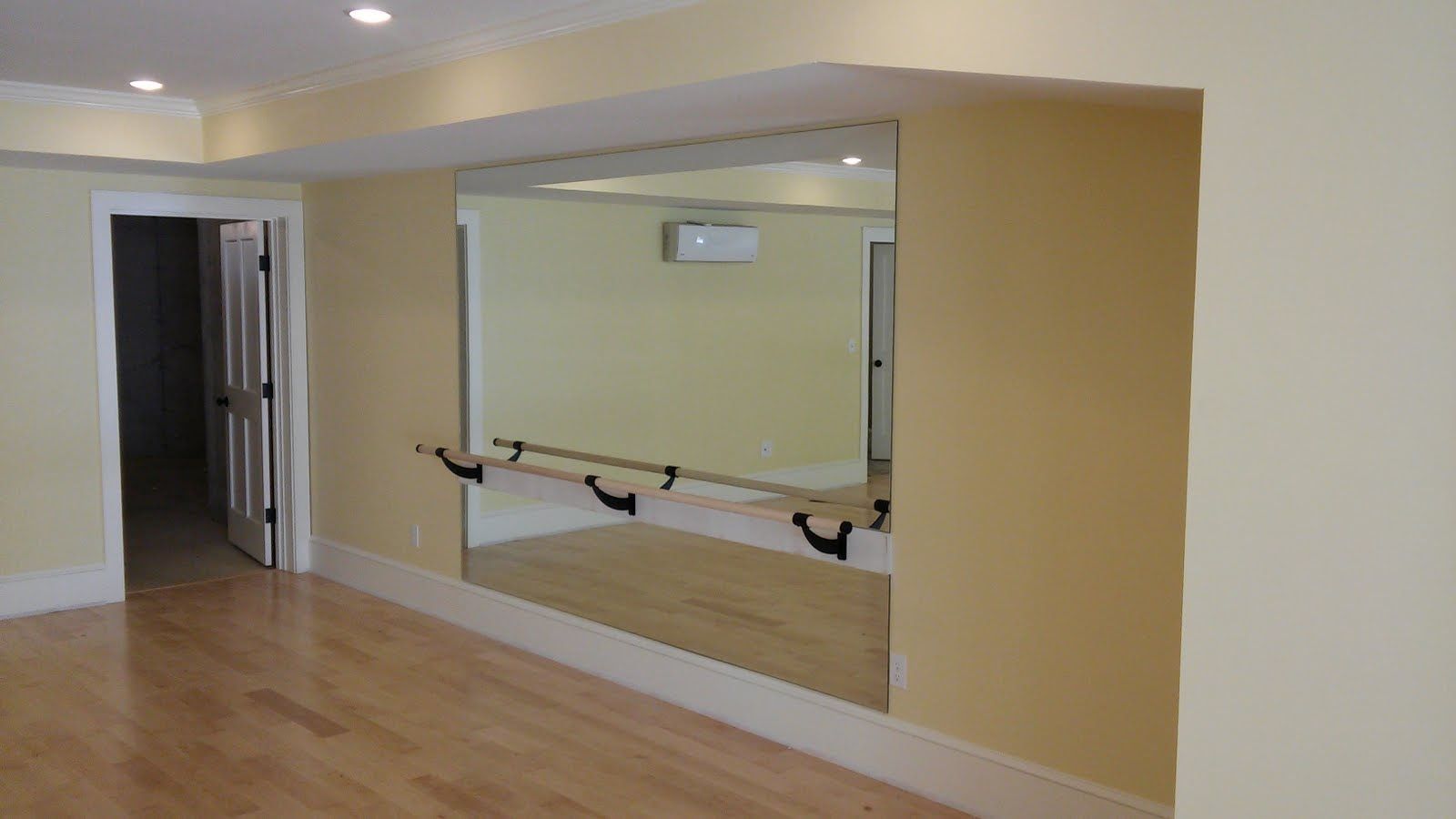 Dance studio with a large mirror, barre, and hardwood floor.