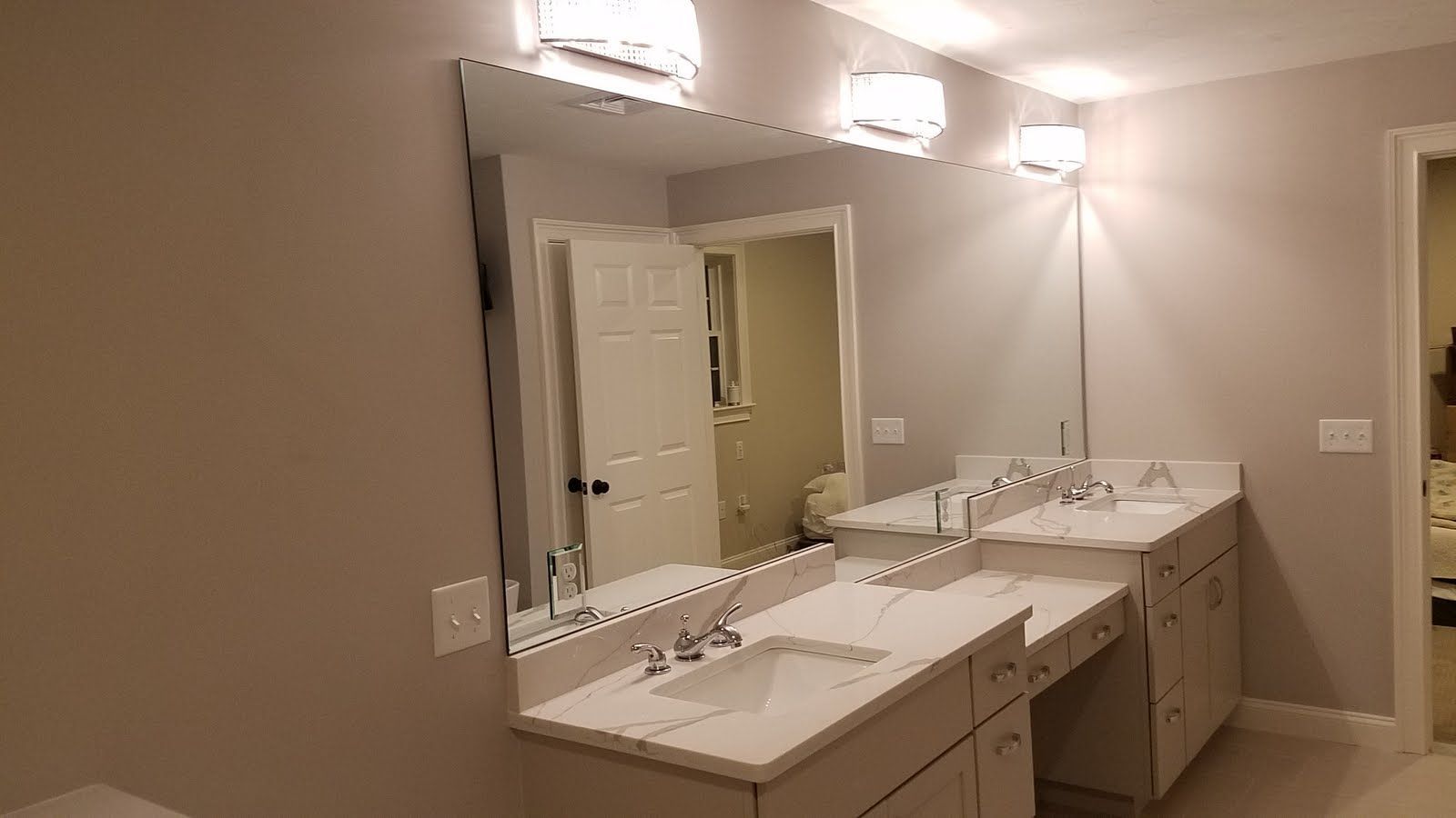 Bathroom with large mirror, two sinks, white countertops, and light fixtures.